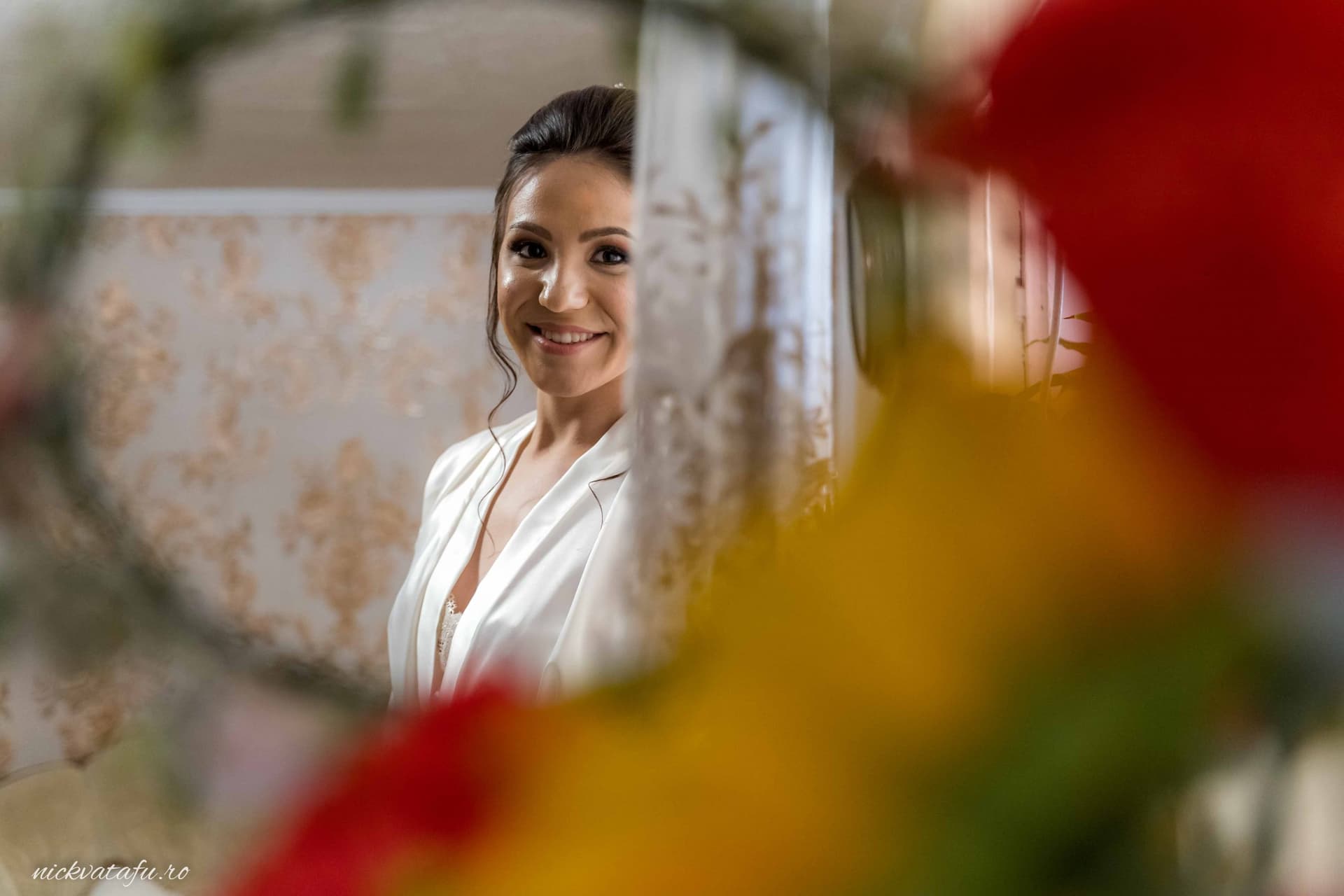 Mireasă zâmbitoare privindu-se în oglindă, emoție și eleganță înainte de ceremonia nunții.