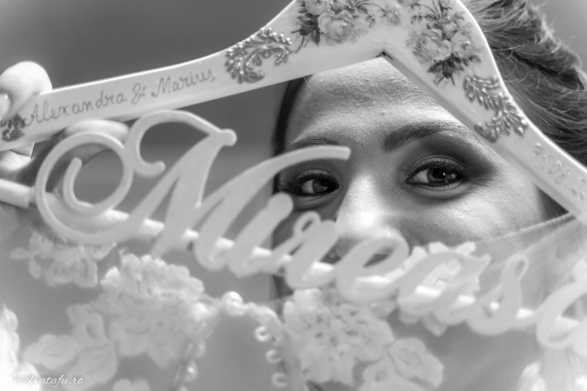 Privind cu emoție spre camera foto, mireasa își prezintă umerașul personalizat cu numele ei, detalii nuntă elegante.