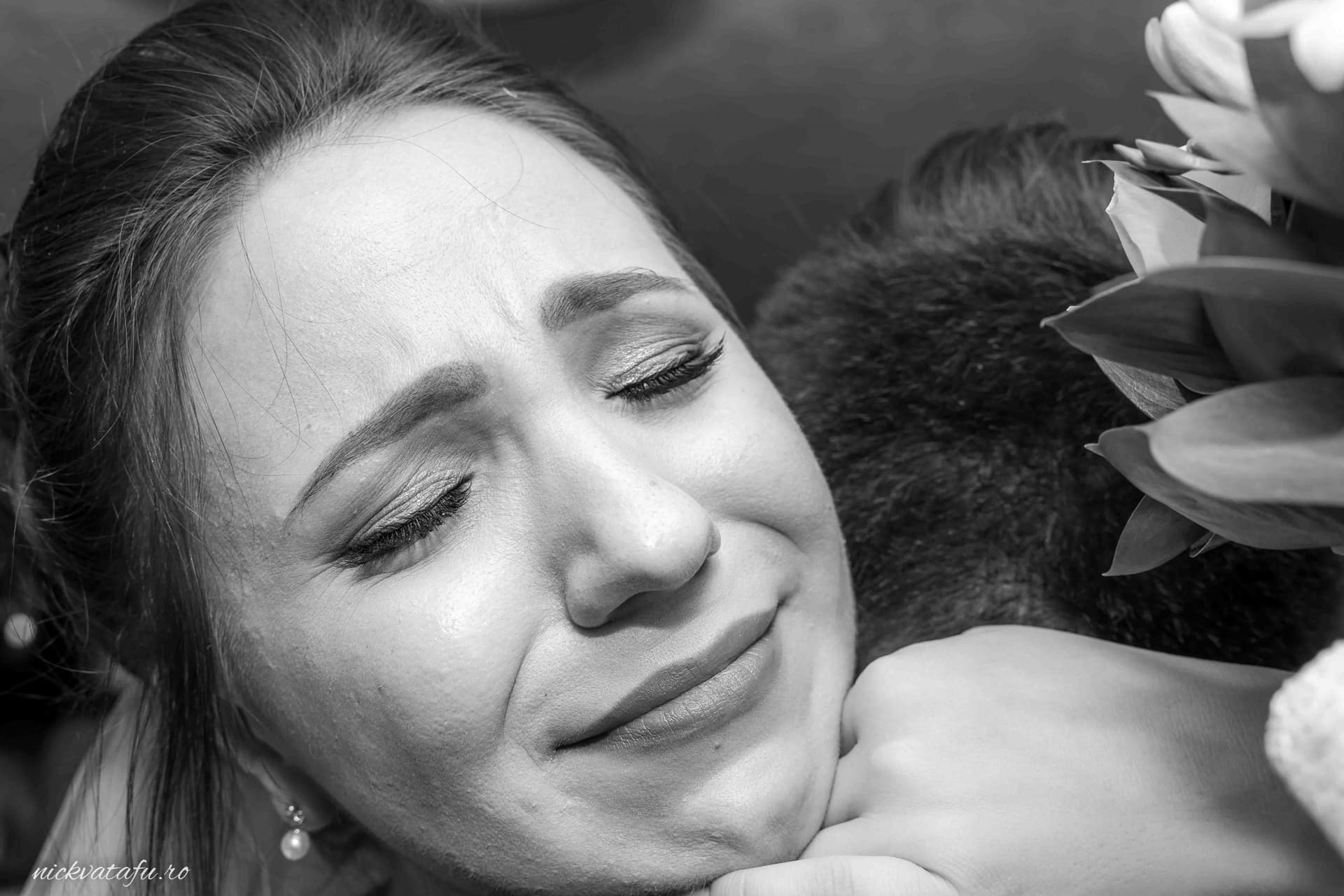 Mireasă emoționată în brațele unei persoane dragi, capturând momentele speciale ale nunții.