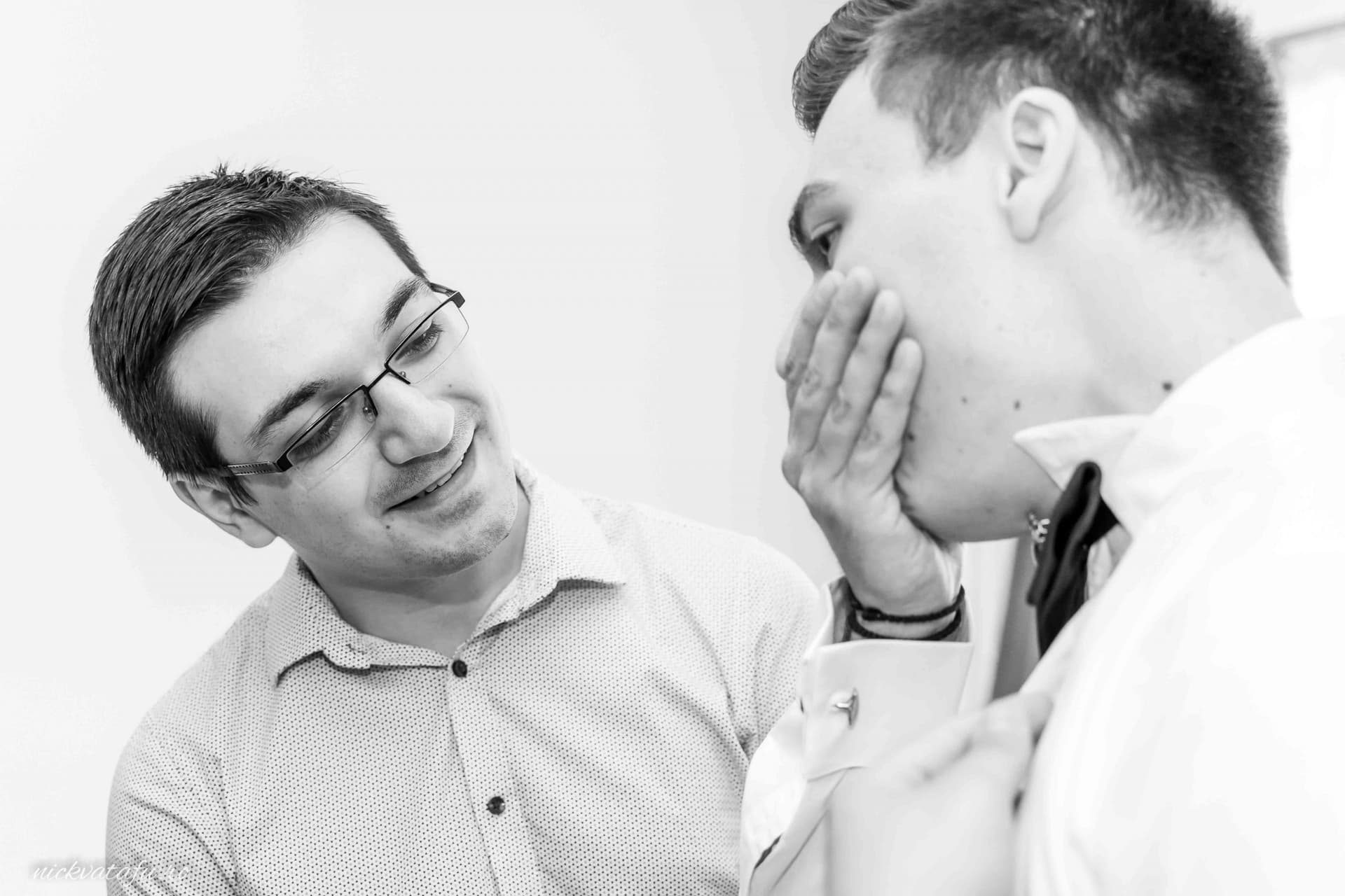 Prieten apropiat ajutându-l pe mire cu emoții înainte de ceremonie, fotografie nuntă alb-negru plină de sinceritate.