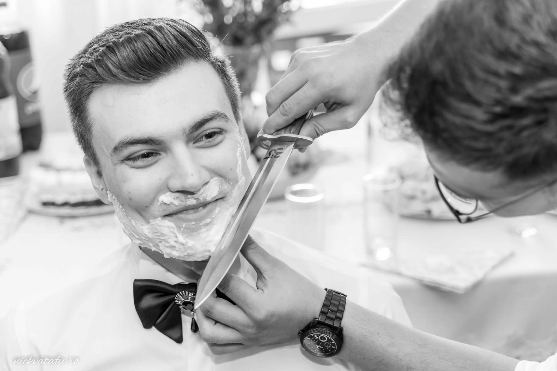 Bărbat zâmbitor în timpul bărbieritului, pregătindu-se pentru nuntă, detalii elegante și emoție în aer.