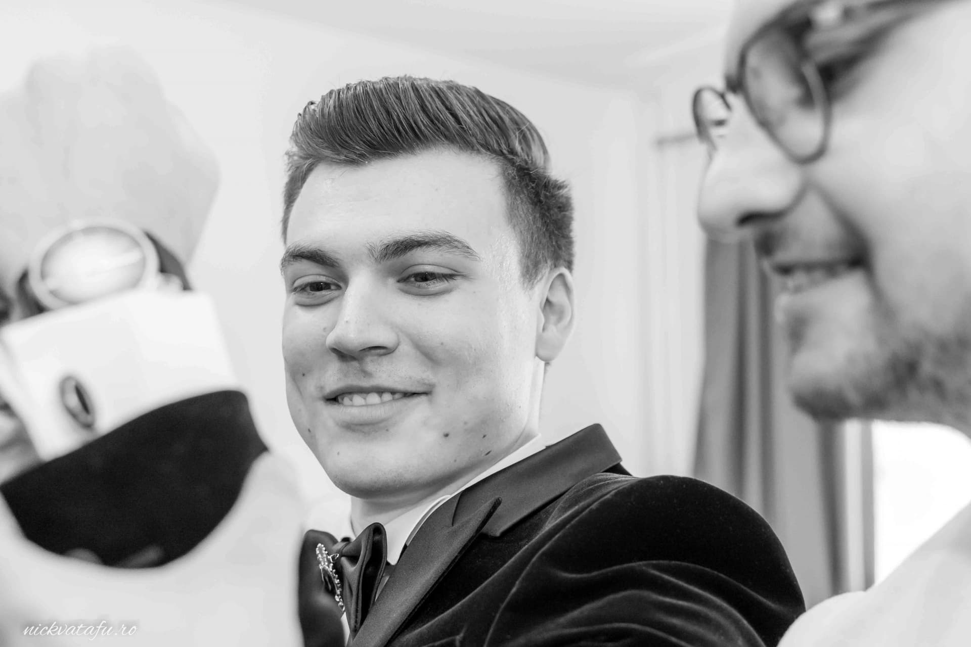 Bărbat zâmbitor îmbrăcat elegant, surprins într-un moment de bucurie la un eveniment festiv.