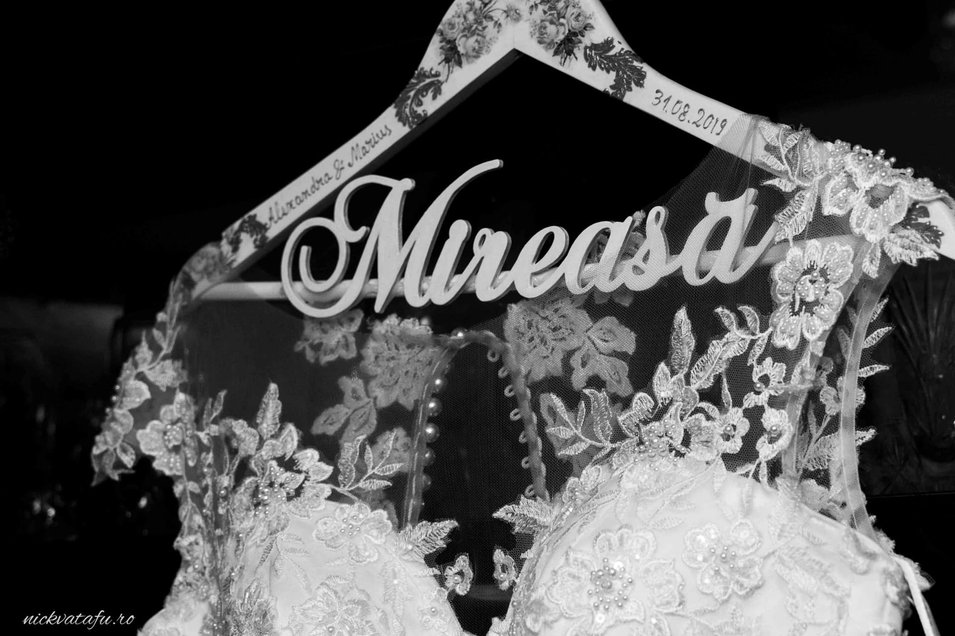 Rochia de mireasă elegantă atârnată pe un umeraș personalizat, detalii delicate și emoție în așteptarea nunții.