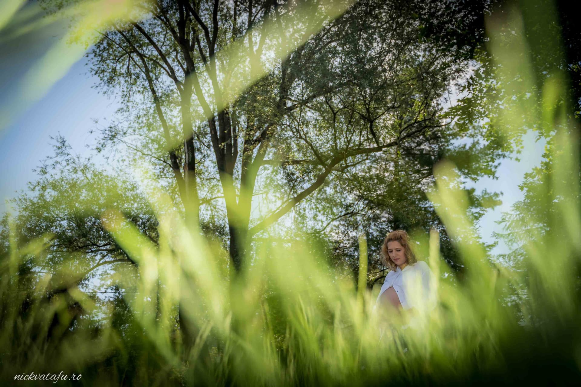 Mireasă zâmbitoare în iarba verde, înconjurată de natură, fotografie de nuntă plină de emoție și frumusețe.