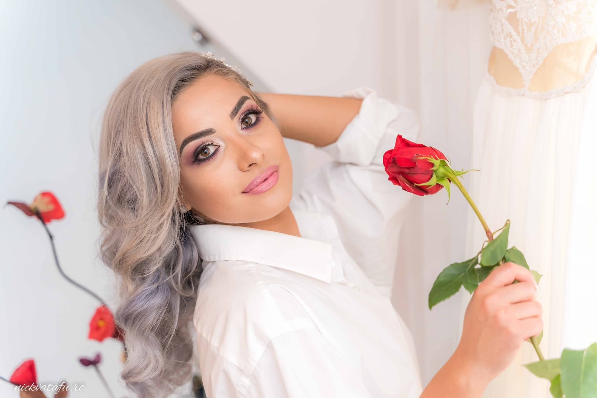 Tânără cu păr gri, zâmbind și ținând o trandafir roșu, surprinsă într-un moment plin de emoție și eleganță.