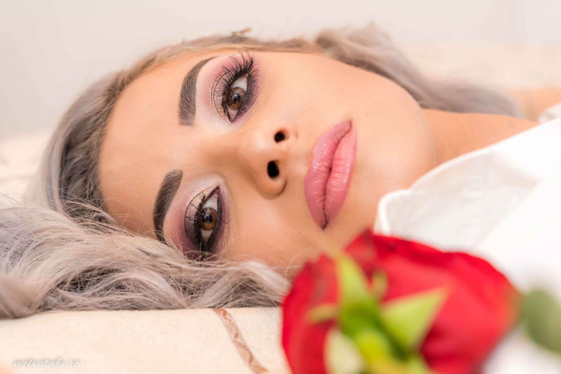 Fată cu părul deschis, privire contemplativă, flori roșii în prim-plan, fotografie elegantă de nuntă.