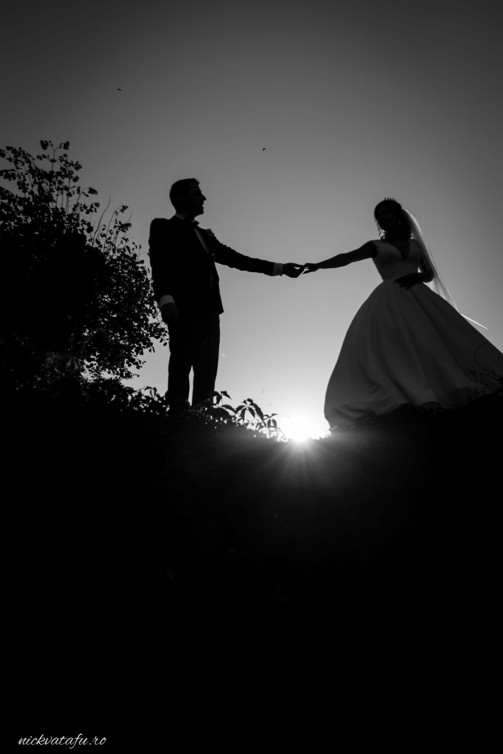 Mire și mireasă ținându-se de mână la apus, fotografie de nuntă plină de emoție și romantism.