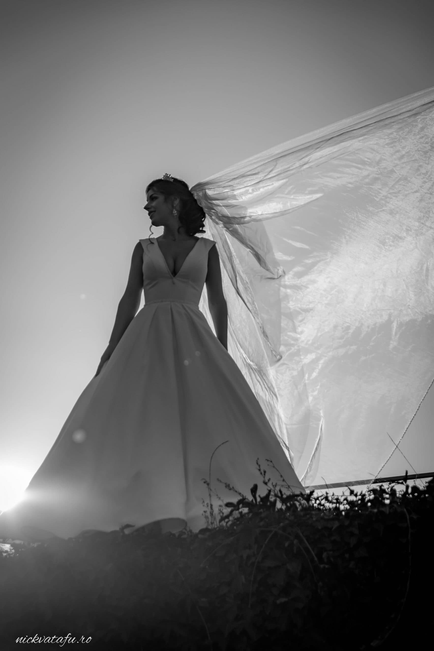 Mireasă elegantă cu voal fluturând în vânt, capturată în lumina soarelui, fotografie nuntă artistică.