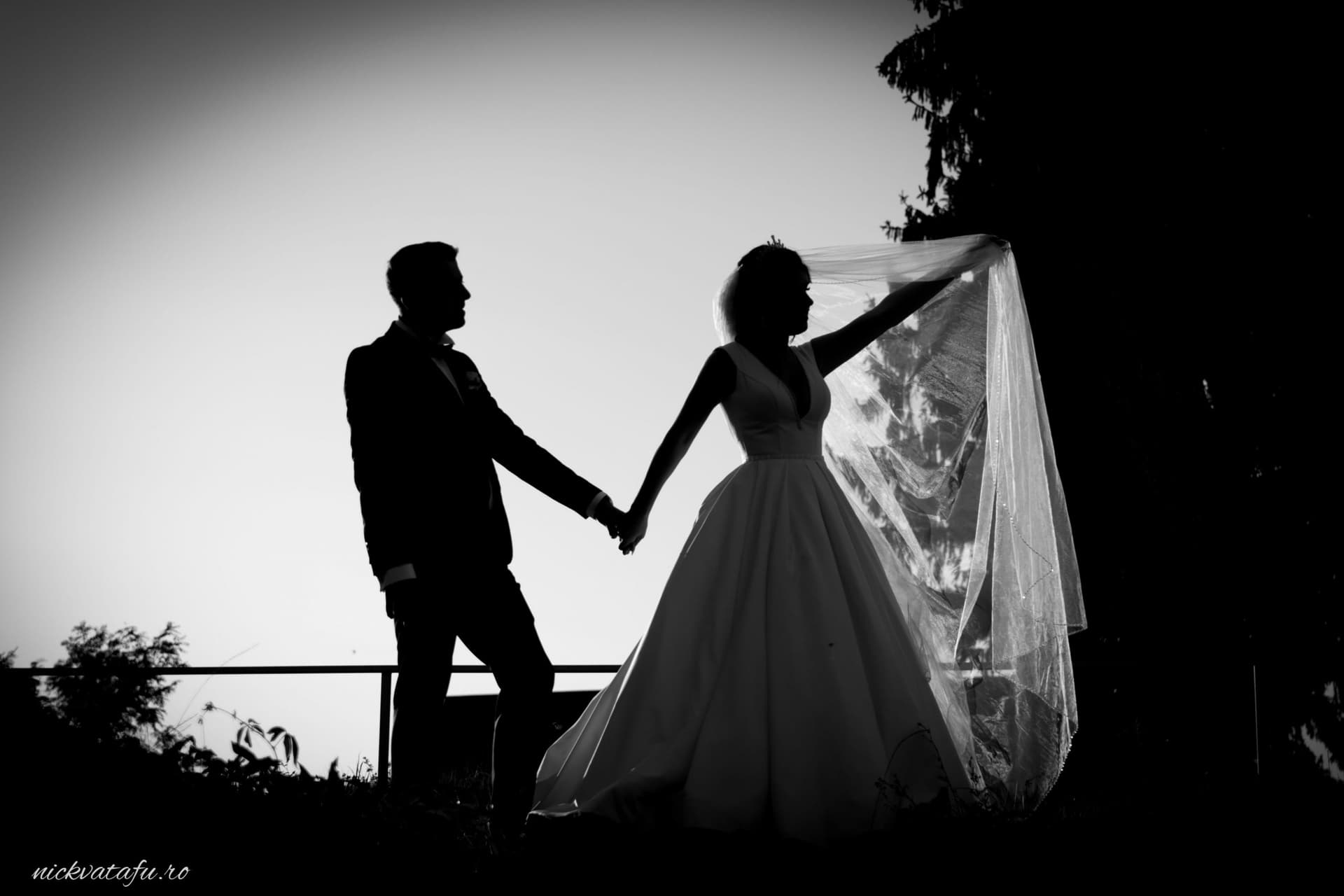 Mire și mireasă ținându-se de mână, cu voalul fluturând, într-o fotografie de nuntă plină de emoție.