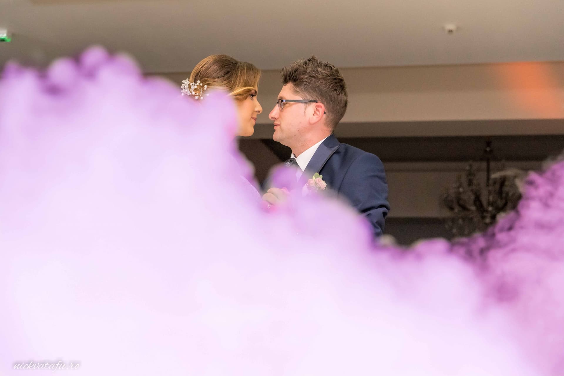 Mire și mireasă privindu-se cu emoție, înconjurați de un fum violet, fotografie de nuntă elegantă.