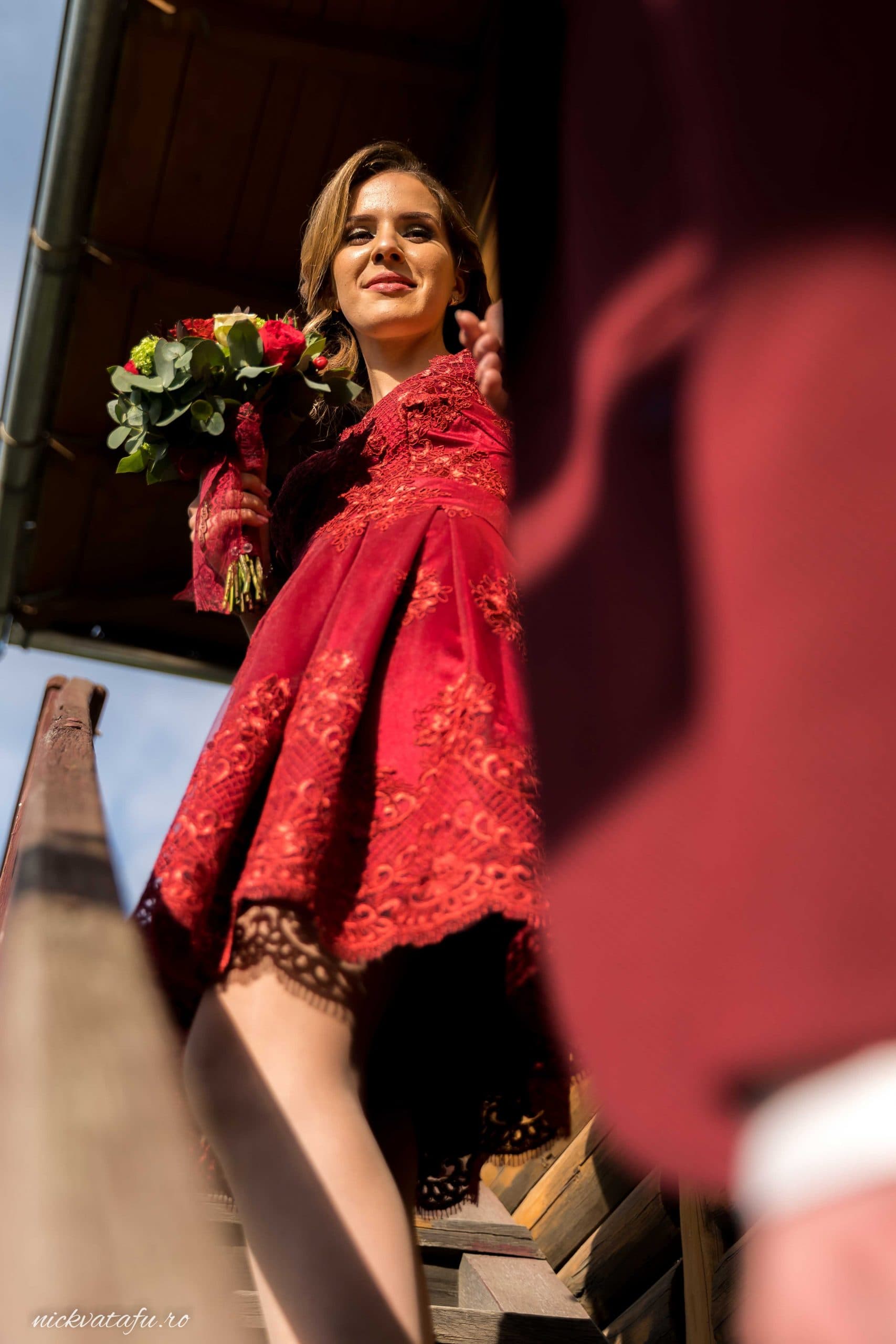 Mireasă zâmbitoare în rochie roșie, urcând treptele, fotografie elegantă de nuntă cu detalii rafinate.