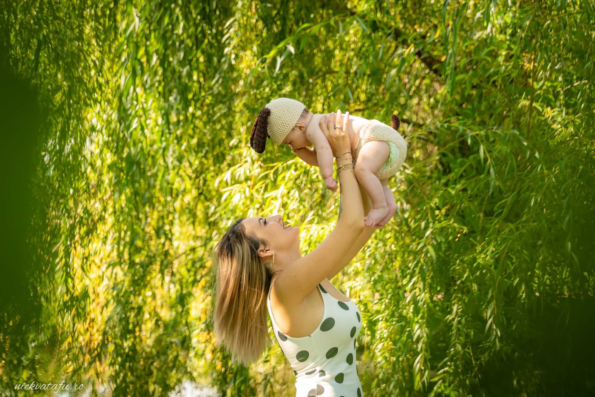 Mama ridică cu bucurie bebelușul într-un cadru natural, capturând o emoție pură și plină de iubire.