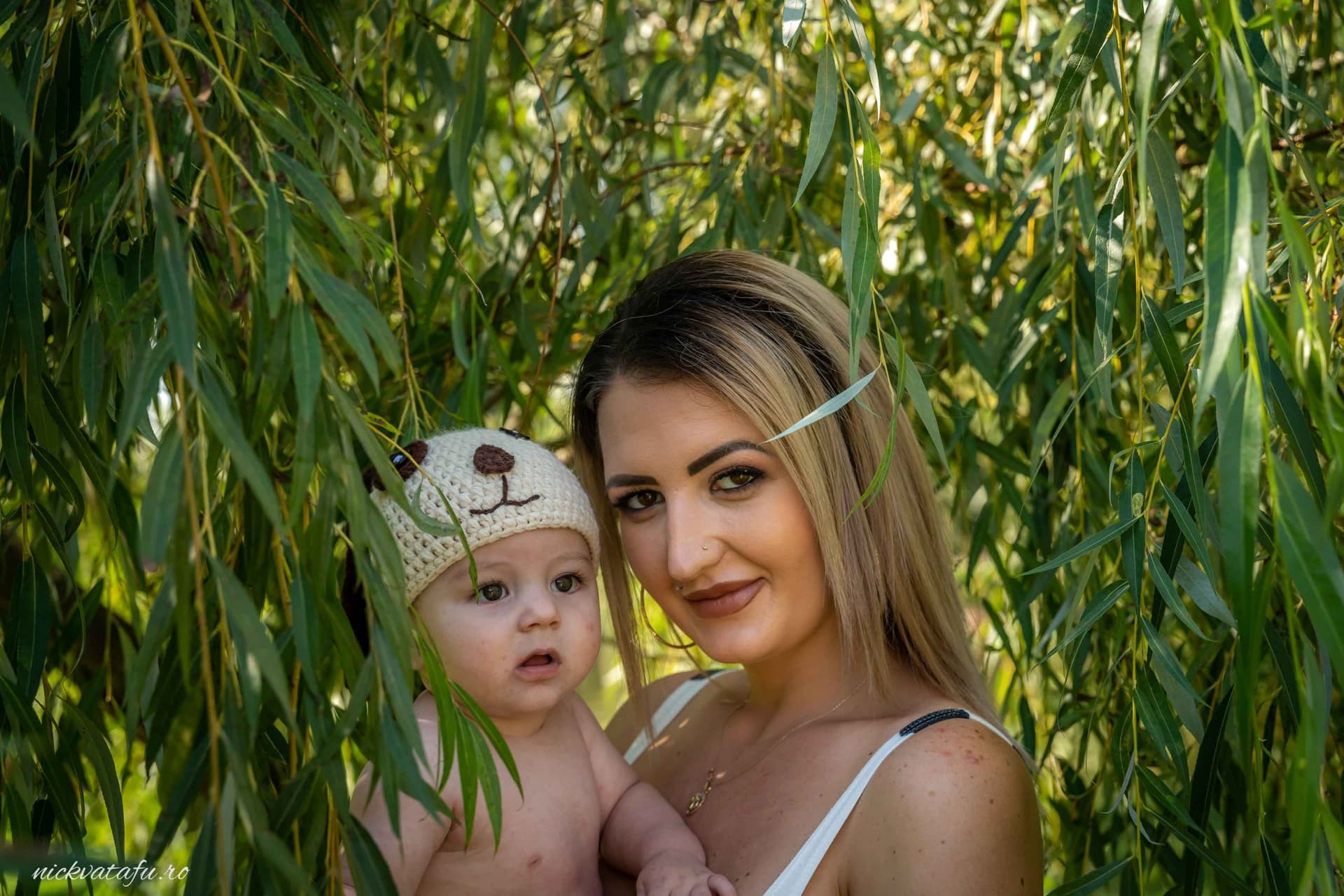 Mamă și copil zâmbind, înconjurați de verdeața unui loc natural, fotografie emoționantă de familie.
