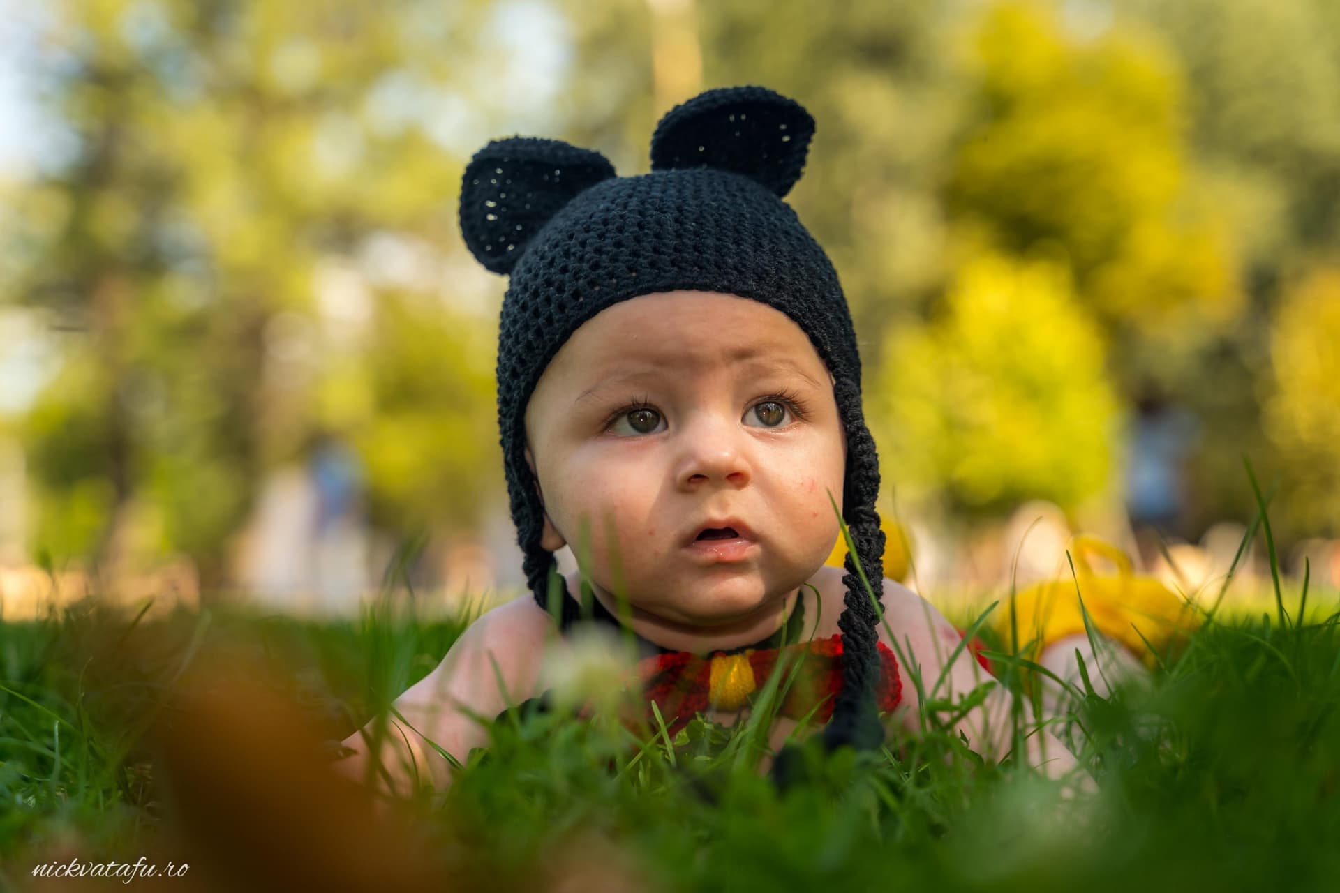 Bebeluș cu pălărie drăguță, zâmbind în iarba verde, evocând emoții de bucurie și inocență.