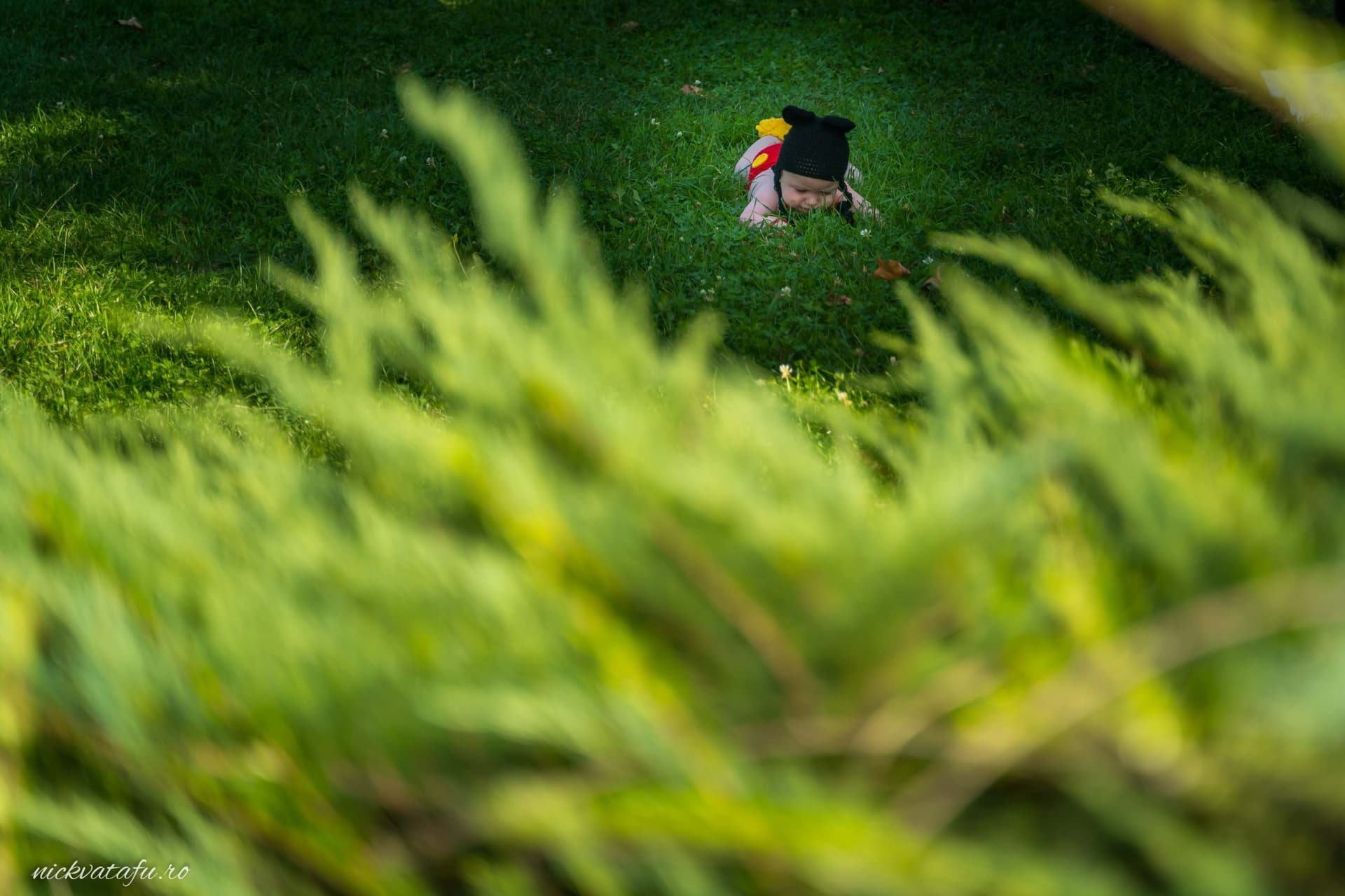 Băiat îmbrăcat în costum de absolvent, zâmbind pe o pajiște verde, fotografie emoționantă de botez în natură.