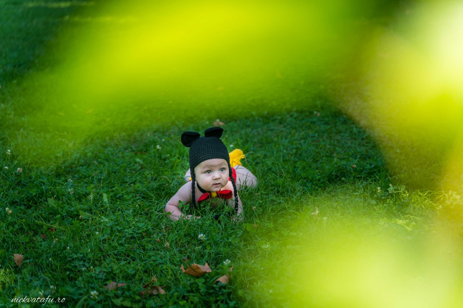 Bebeluș zâmbitor că crawling pe iarbă, purtând o pălărie drăguță, într-un cadru plin de emoție și veselie.