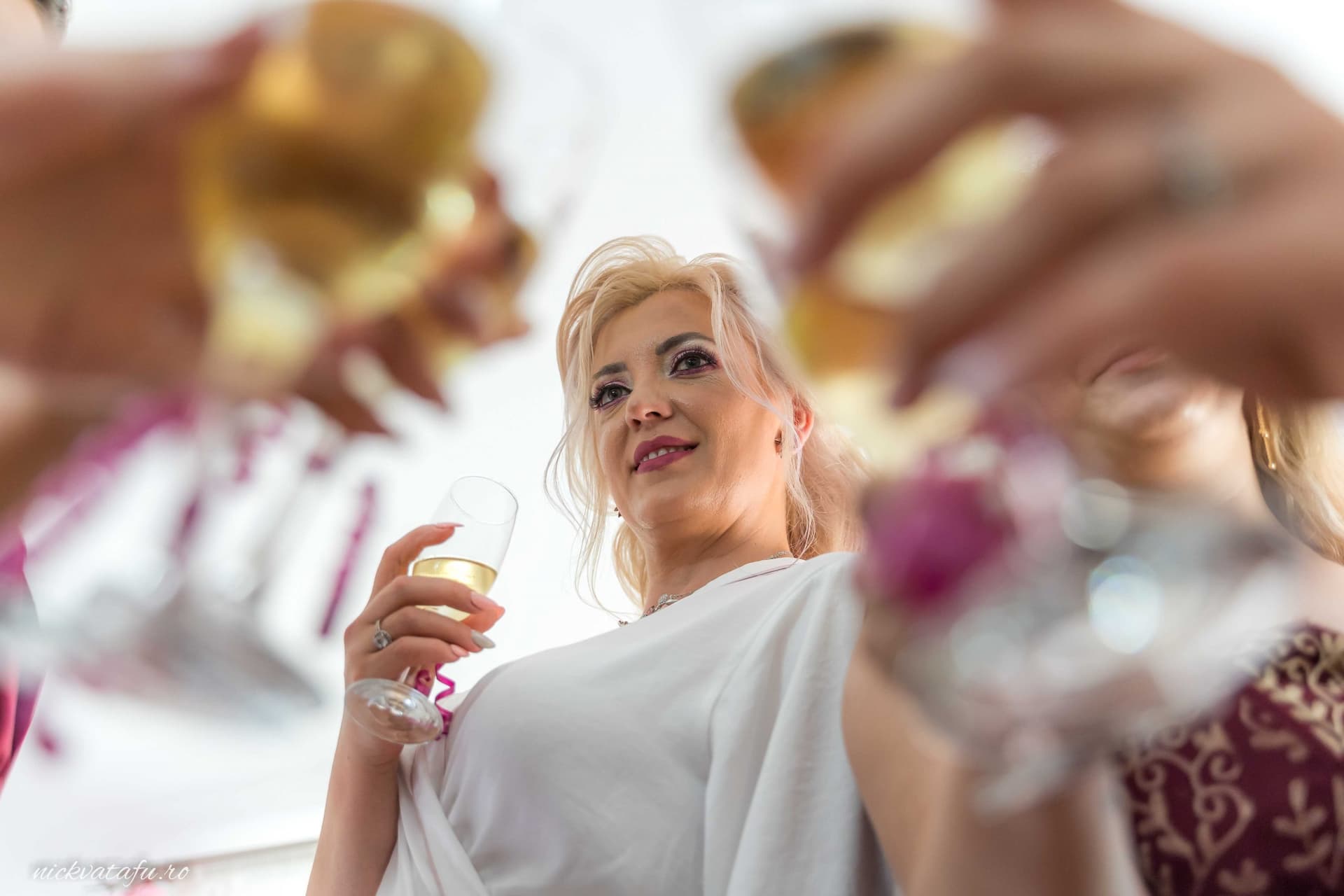 Mireasă zâmbitoare, cu un pahar de șampanie în mână, în mijlocul unei atmosfere festive de nuntă.