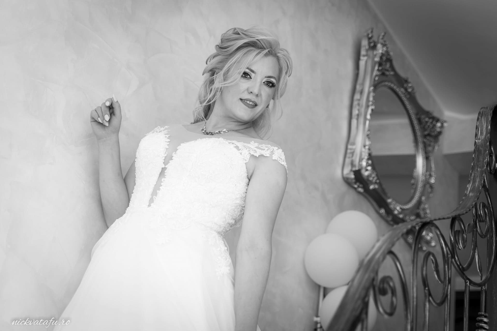 Mireasă elegantă în rochie albă, zâmbind pe scări, pregătiri pentru fotografie de nuntă.