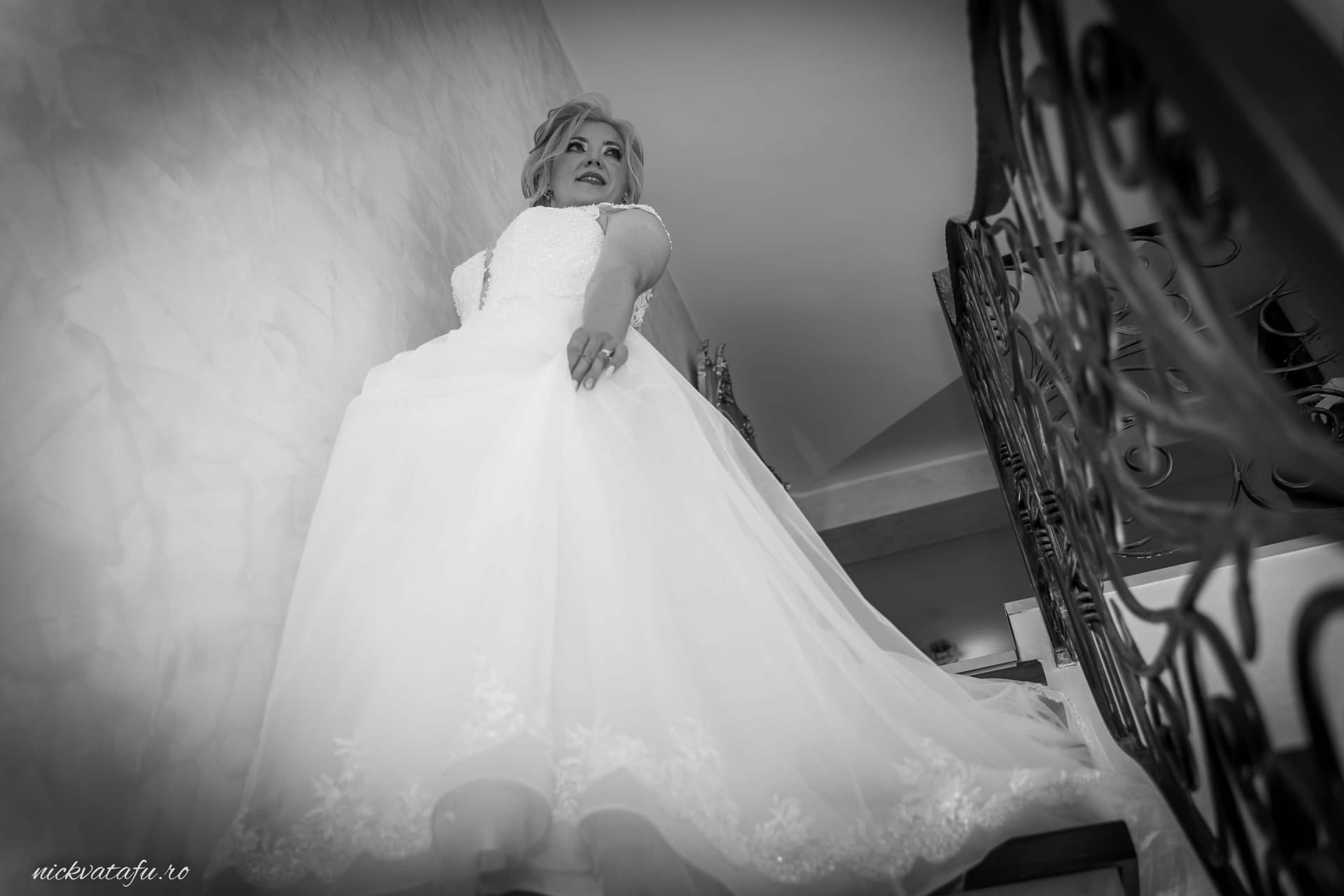 Mireasă elegantă pe scări, zâmbind cu emoție înainte de ceremonie, fotografie nuntă în alb-negru.
