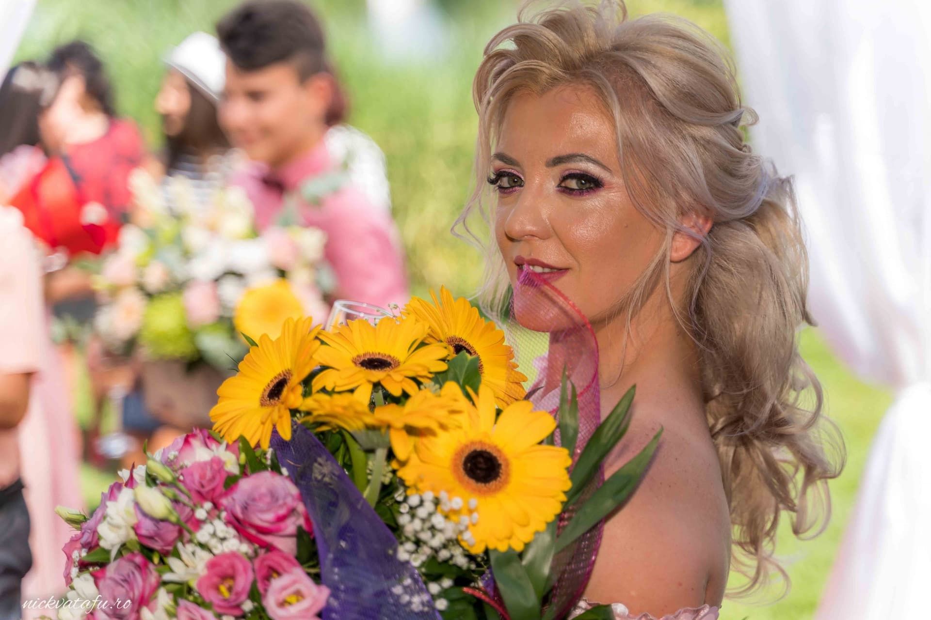 Mireasă zâmbitoare, cu un buchet de flori colorate, surprinsă într-un moment plin de emoție la o nuntă.