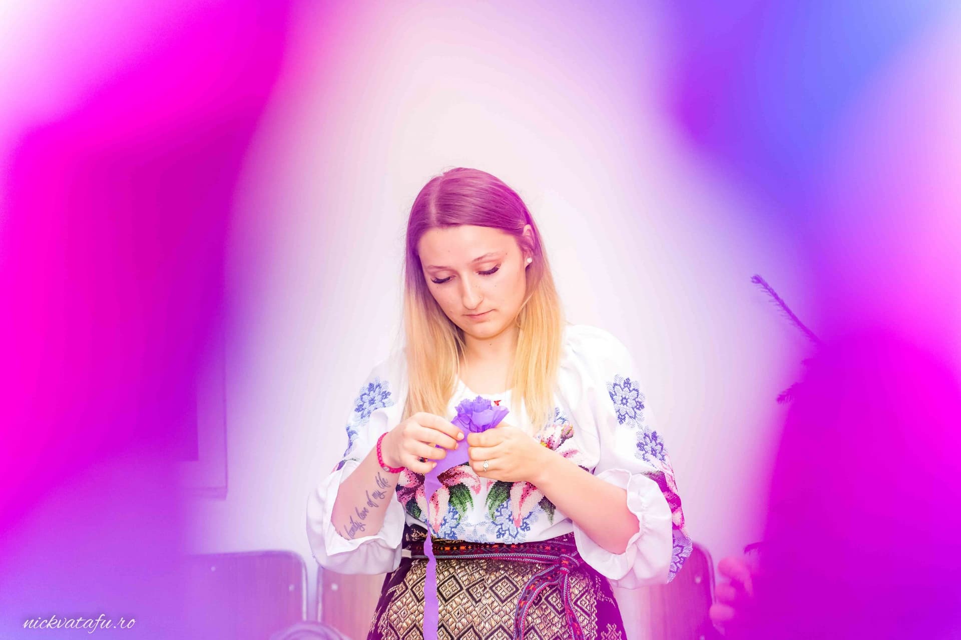 Fată îmbrăcată în costum popular, pregătind un buchet de flori, emoție și tradiție în atmosfera unei nunți.