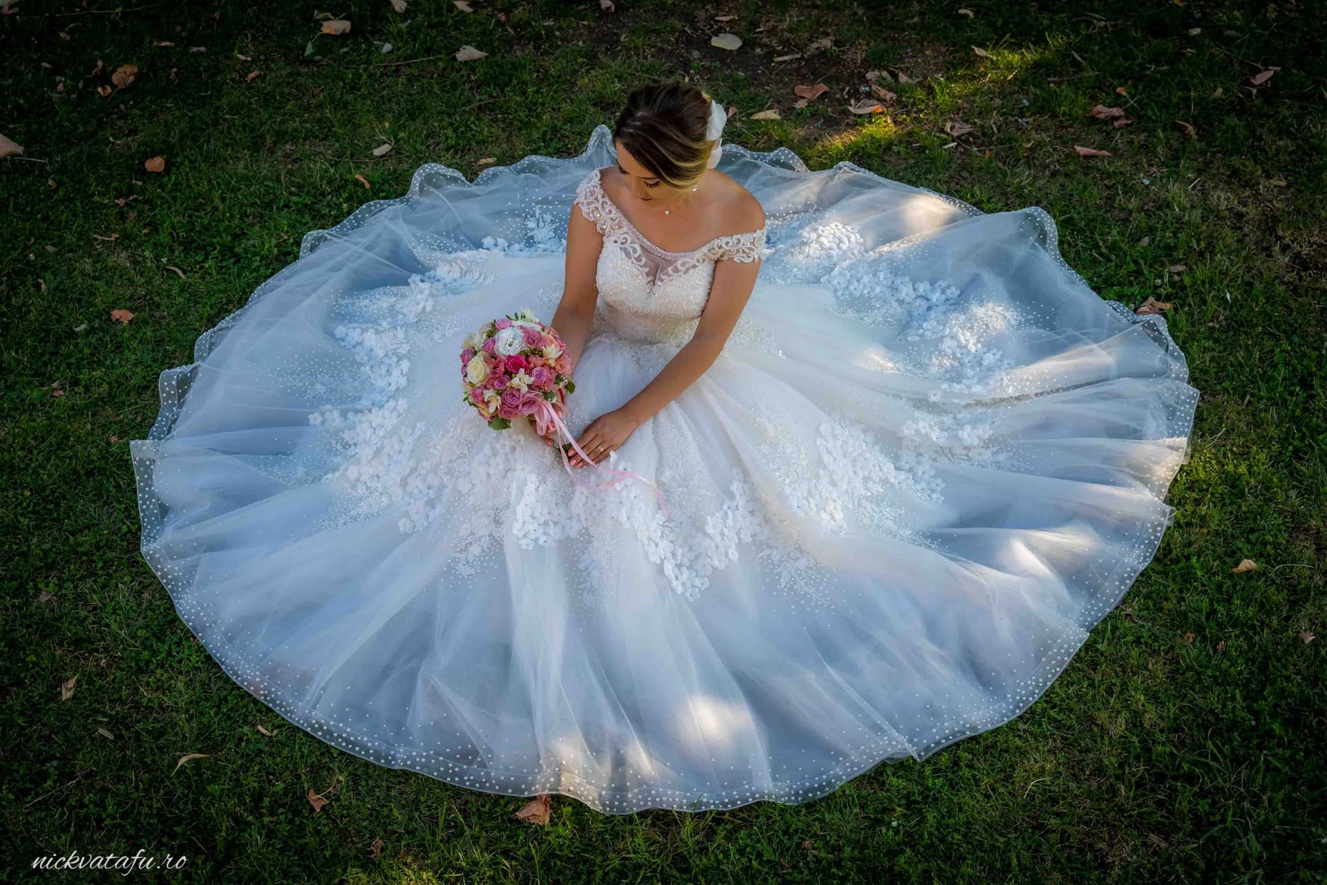 Mireasă contemplativă, cu buchet în mână, îmbrăcată în rochie elegantă, pe iarba verde, detalii nuntă.