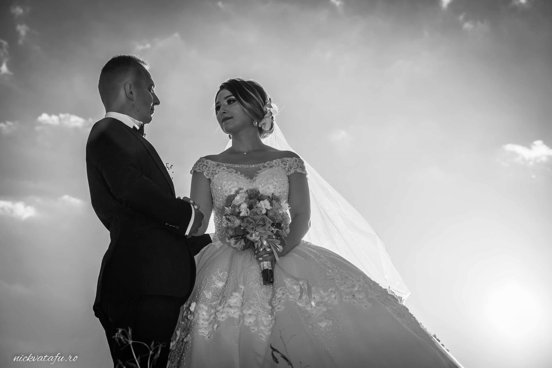 Mire și mireasă privindu-se cu emoție, fotografia de nuntă surprinde un moment intim în lumina apusului.