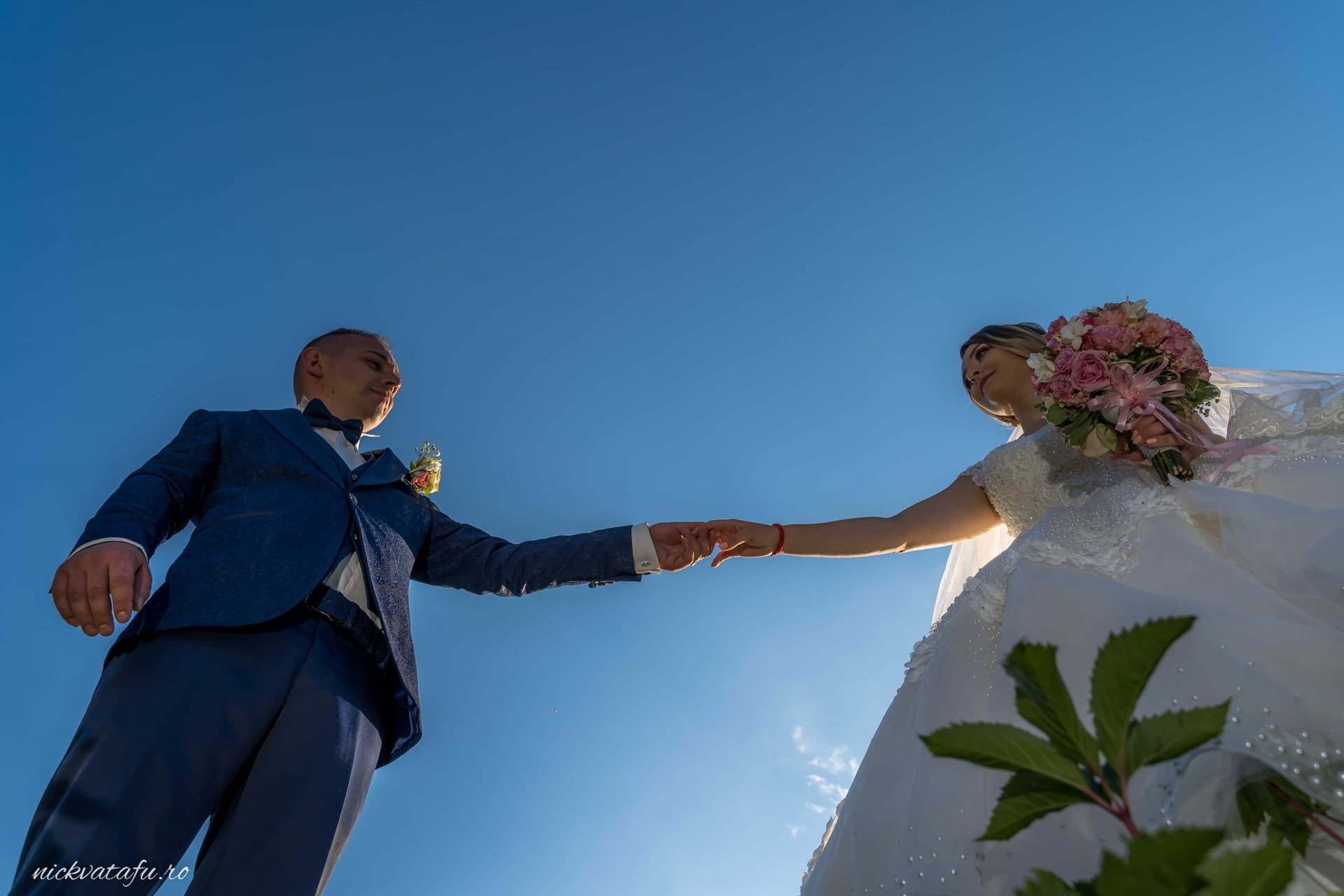 Mire și mireasă ținându-se de mână sub un cer senin, fotografie de nuntă plină de emoție și romantism.