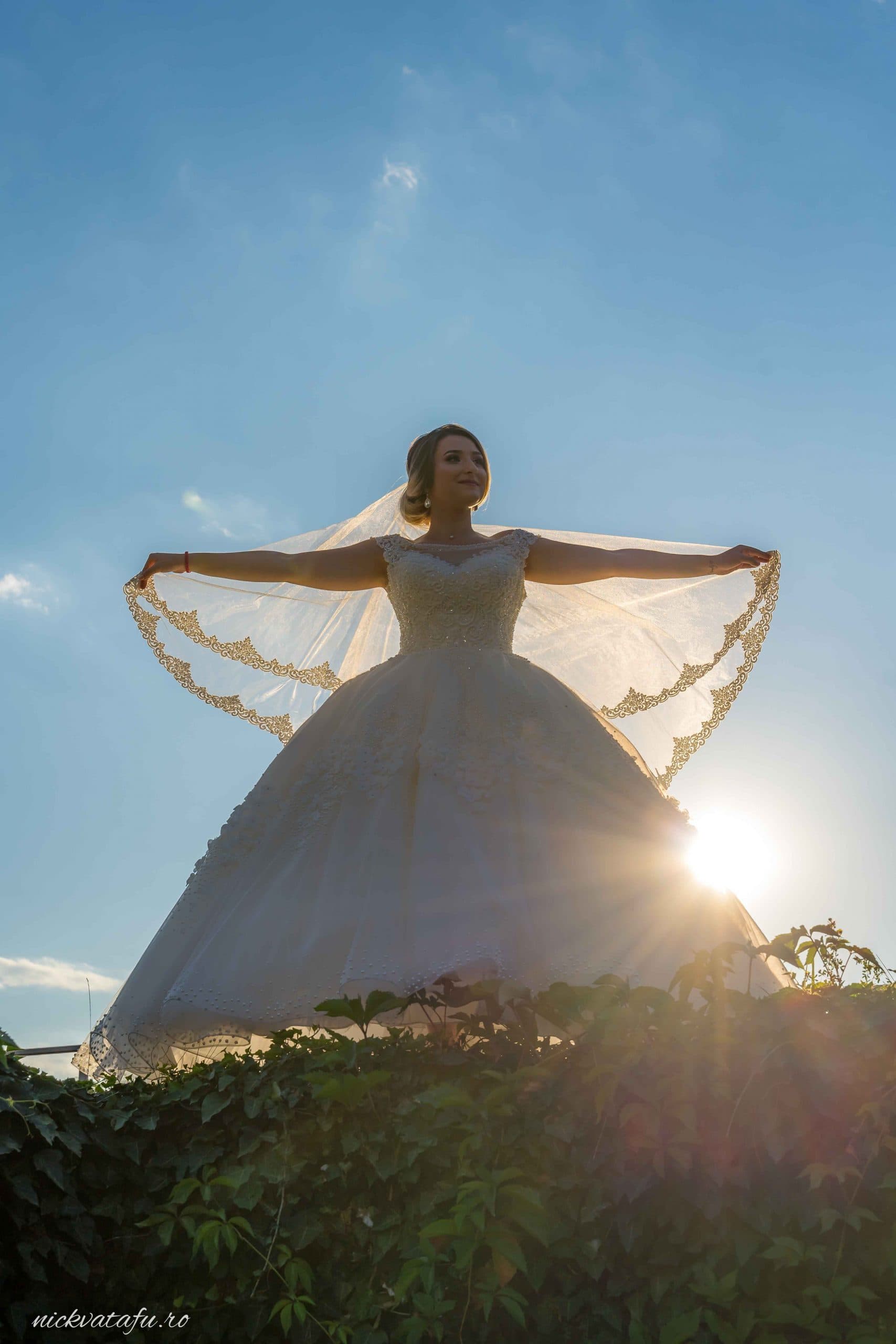 Mireasă strălucind în lumina soarelui, cu voalul fluturând, fotografie de nuntă plină de emoție.