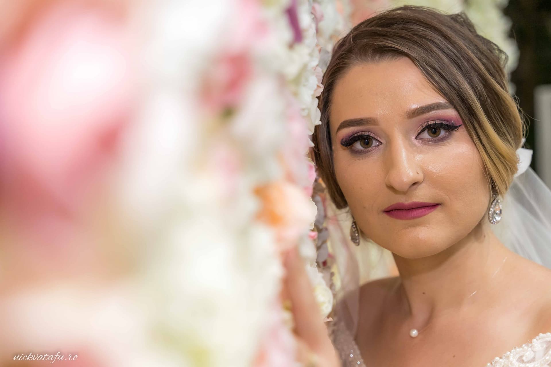 Mireasă cu un zâmbet emoționant, înconjurată de flori delicate, fotografie nuntă plină de eleganță.