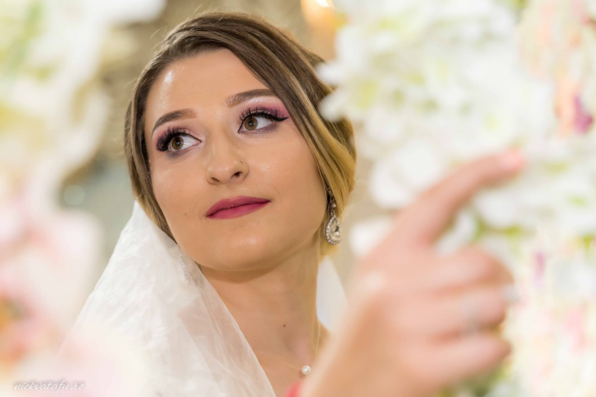 Mireasă cu un zâmbet subtil, purtând voal și flori, emanând emoție în cadrul unei fotografii de nuntă.