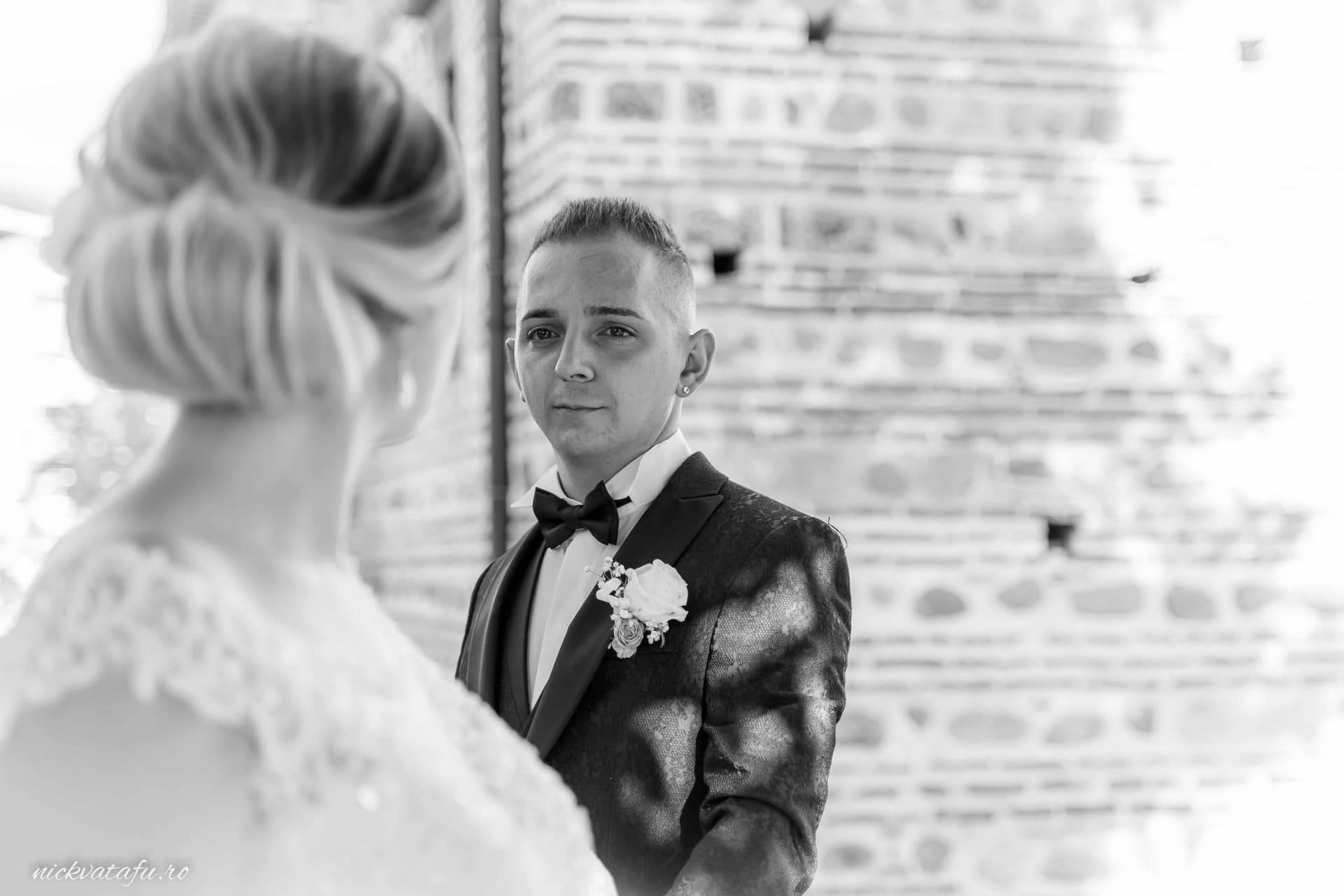 Mirele privește emoționat spre mireasă, într-un cadru elegant, fotografie de nuntă cu detalii rafinate.
