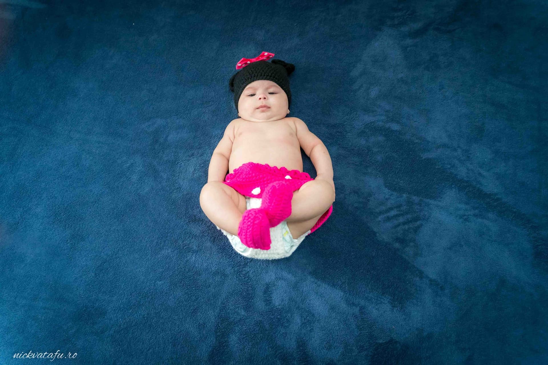 Bebeluș adorabil îmbrăcat în roz, relaxat pe o pătură albastră, fotografie emoționantă de botez.