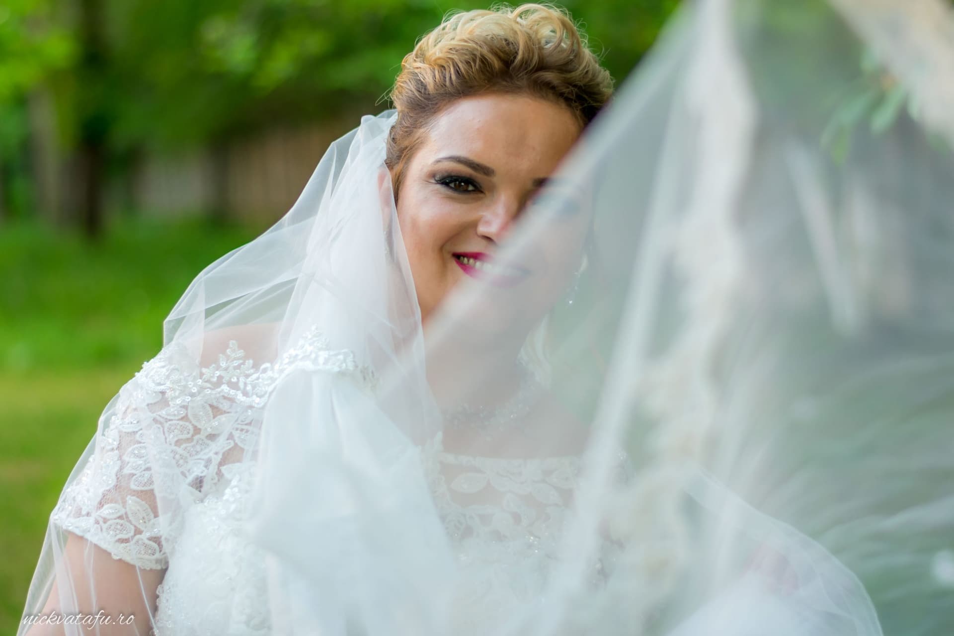 Mireasă zâmbitoare, cu voal delicat, surprinsă într-un moment de emoție, fotografie nuntă în natură.