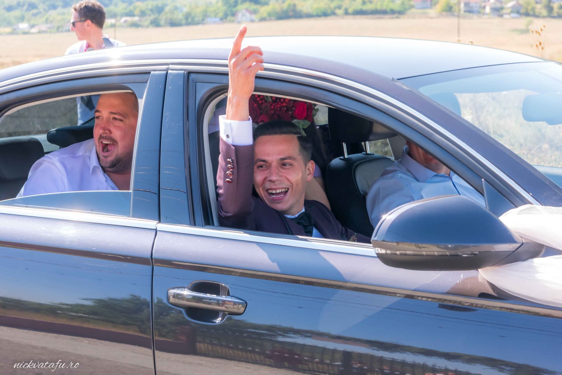 Bărbat zâmbitor dintr-o mașină, sărbătorind cu prietenii, fotografie nuntă plină de emoție și bucurie.