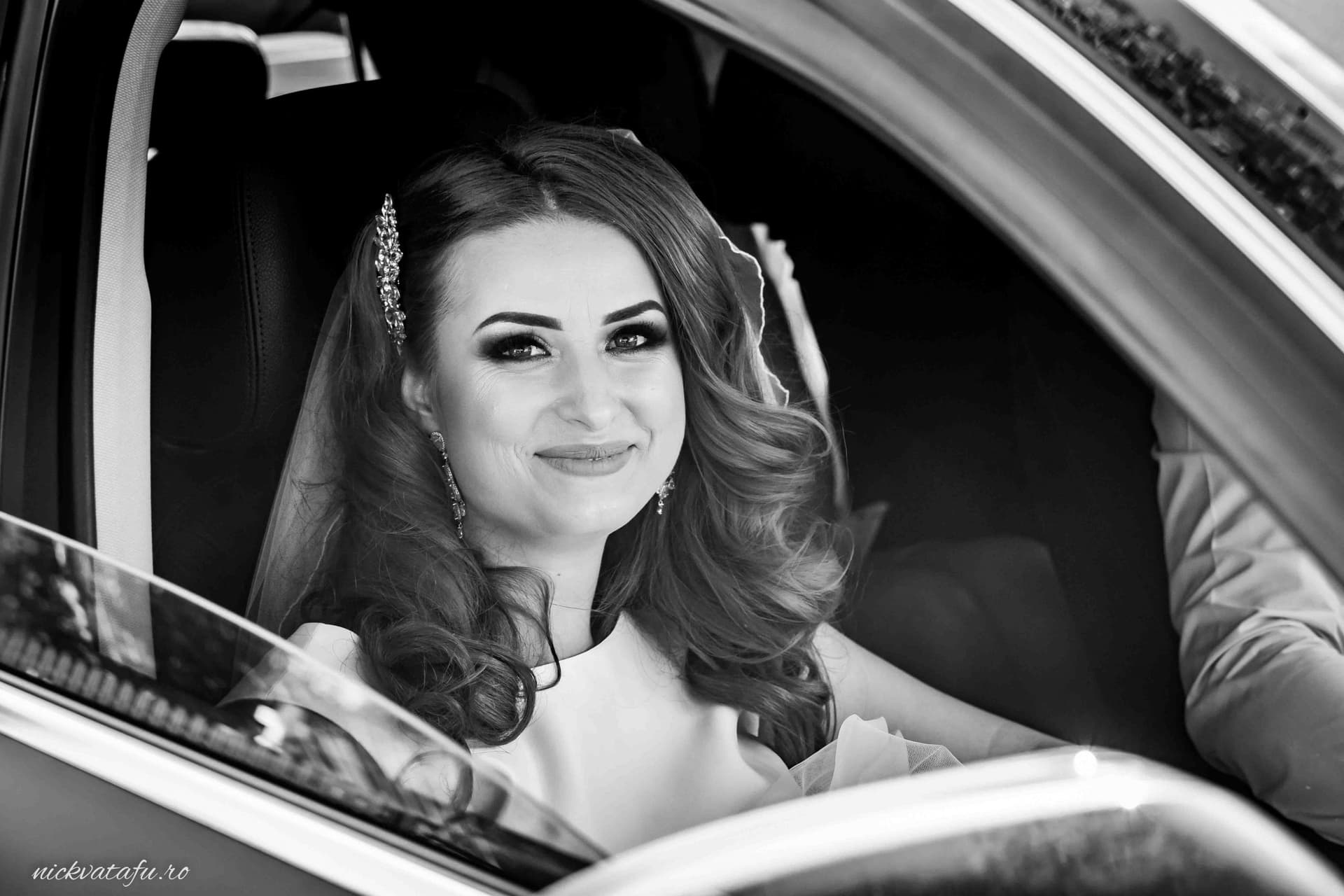 Mireasă zâmbitoare în mașină, pregătindu-se pentru ceremonia de nuntă, fotografie elegantă în alb-negru.