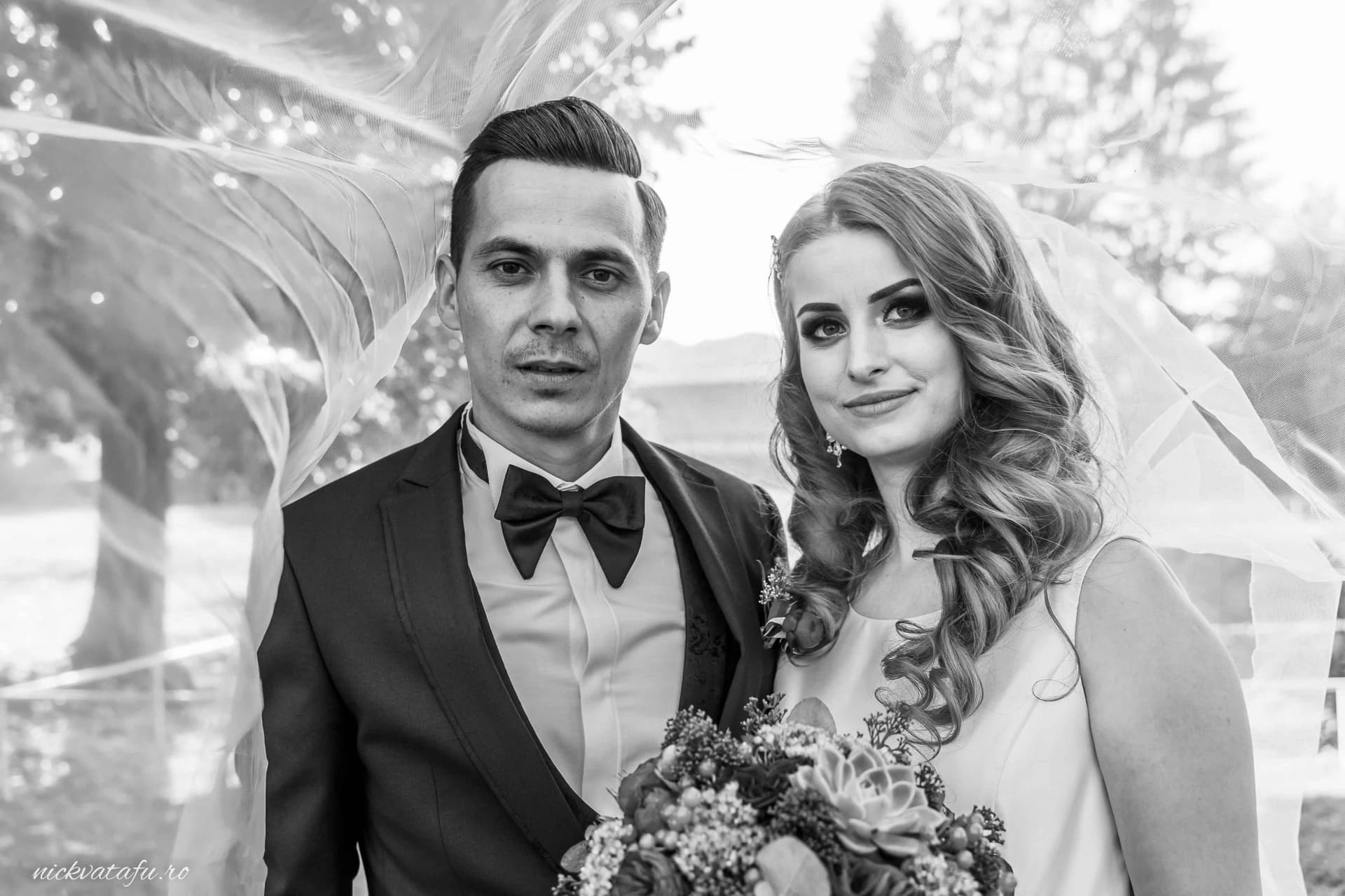 Mire și mireasă zâmbind fericiți, îmbrăcați elegant, în fotografie de nuntă cu fond natural.