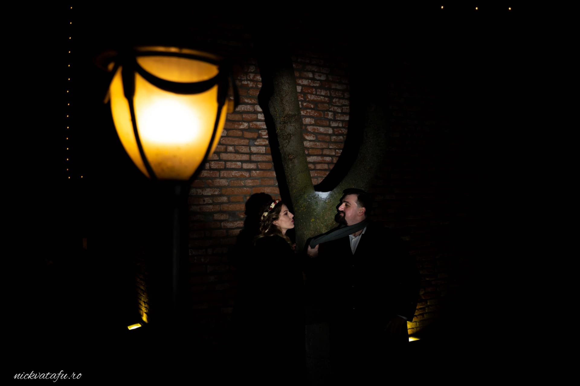 Cuplu zâmbind sub o lampă vintage, fotografie de nuntă cu emoție, în decor urban nocturn.