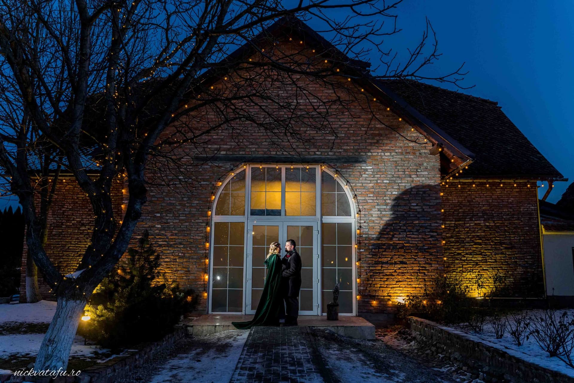 Mire și mireasă în fața unei clădiri iluminate, creând o atmosferă romantică într-o fotografie de nuntă nocturnă.