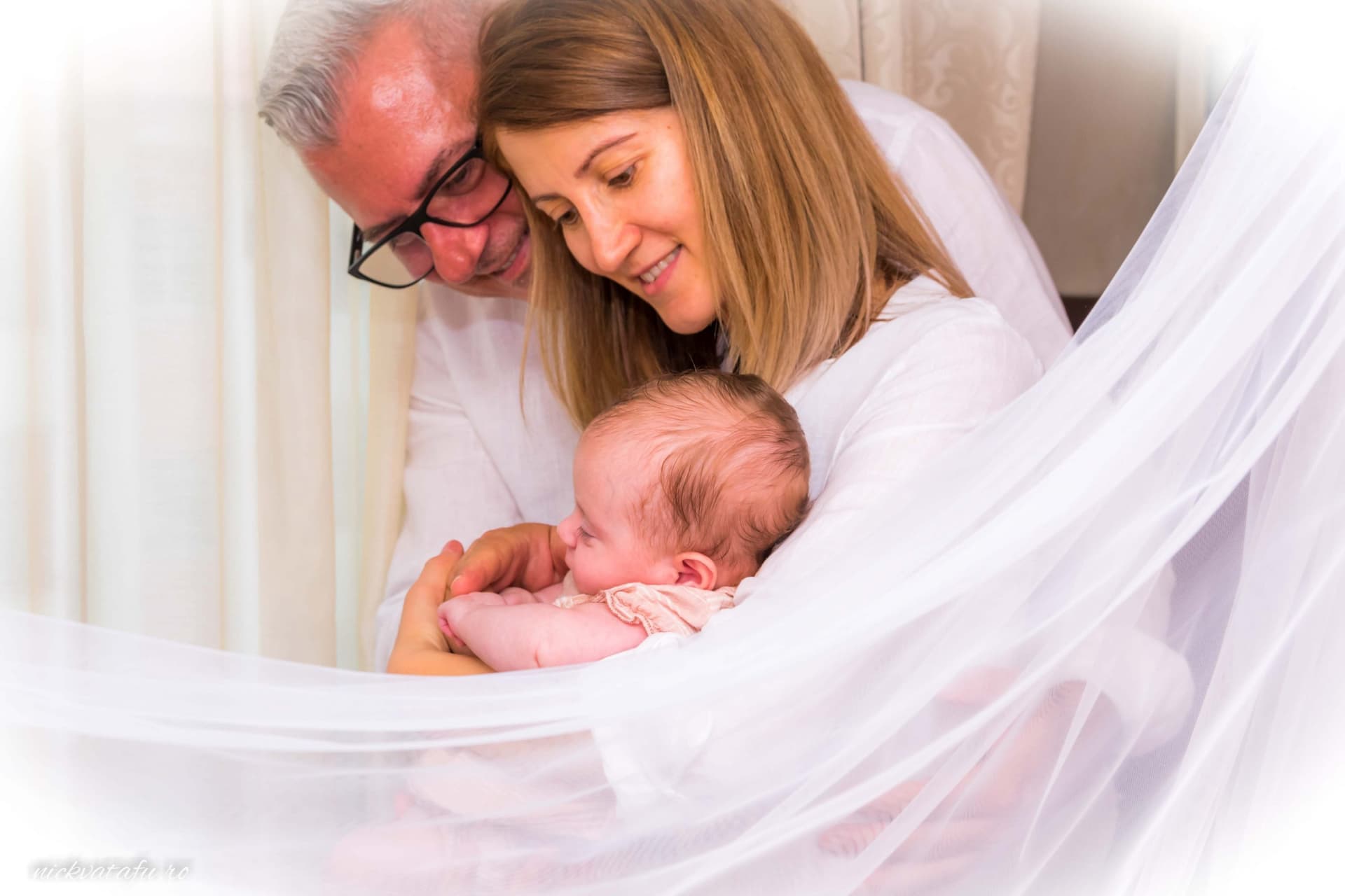 Părinți emoționați țin în brațe un bebeluș adorabil, fotografia de botez surprinzând dragostea familială.