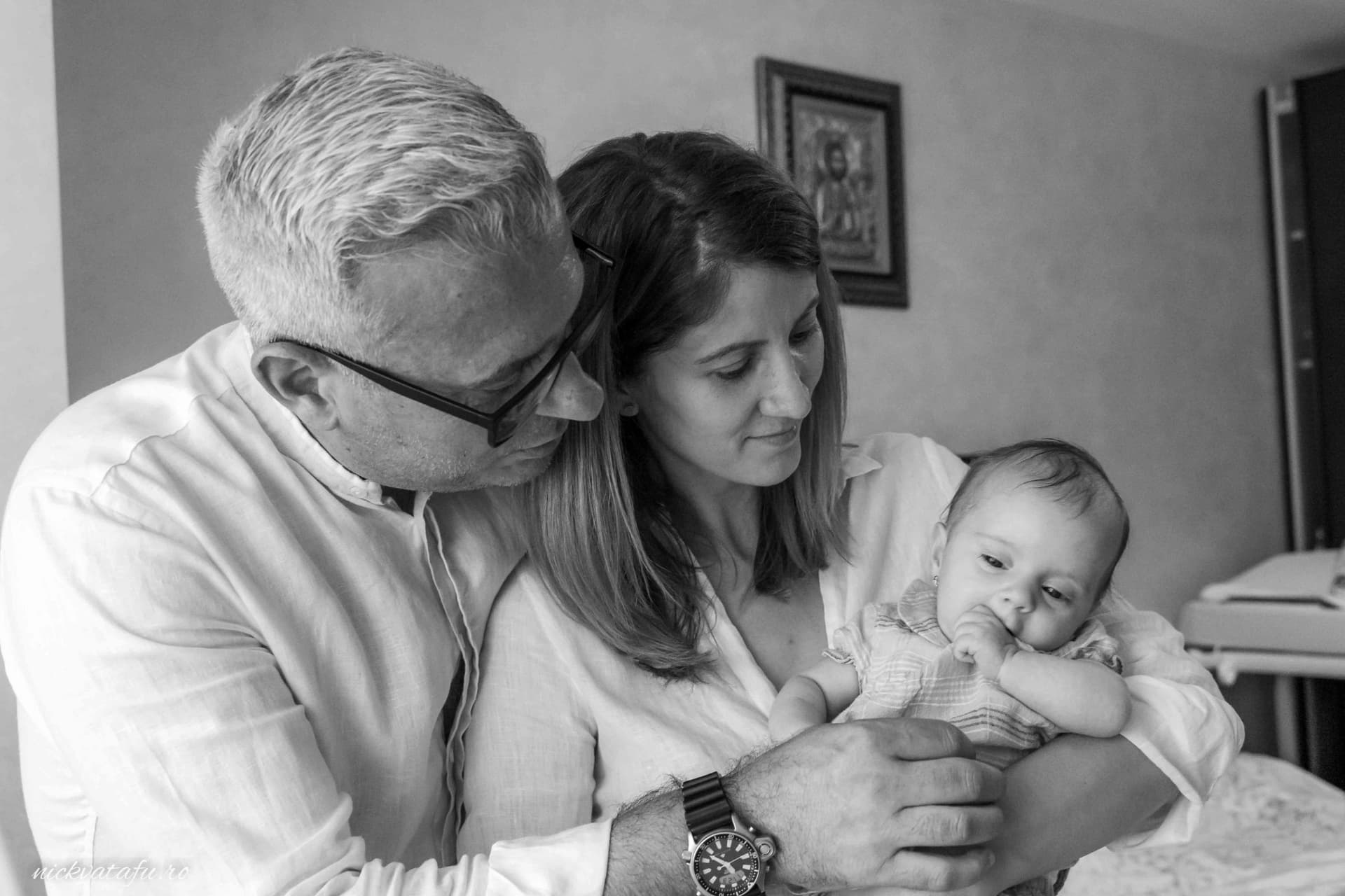 Familie unită, părinți care își țin copilul în brațe, emoție și bucurie într-o fotografie de botez.