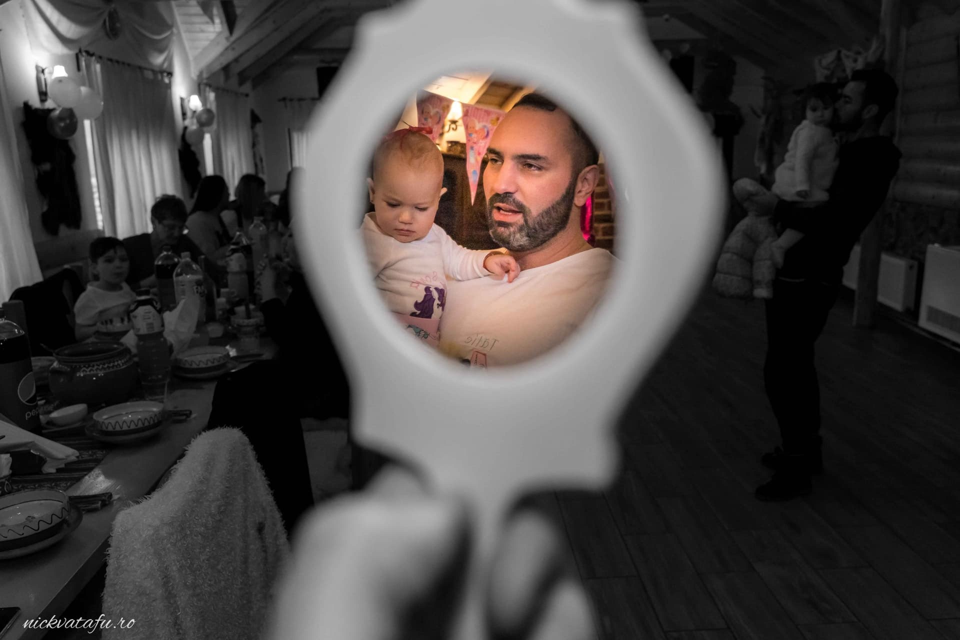 Bărbat cu o expresie emoționată ținând un copil, surprinși printr-o oglindă, la o petrecere de familie.
