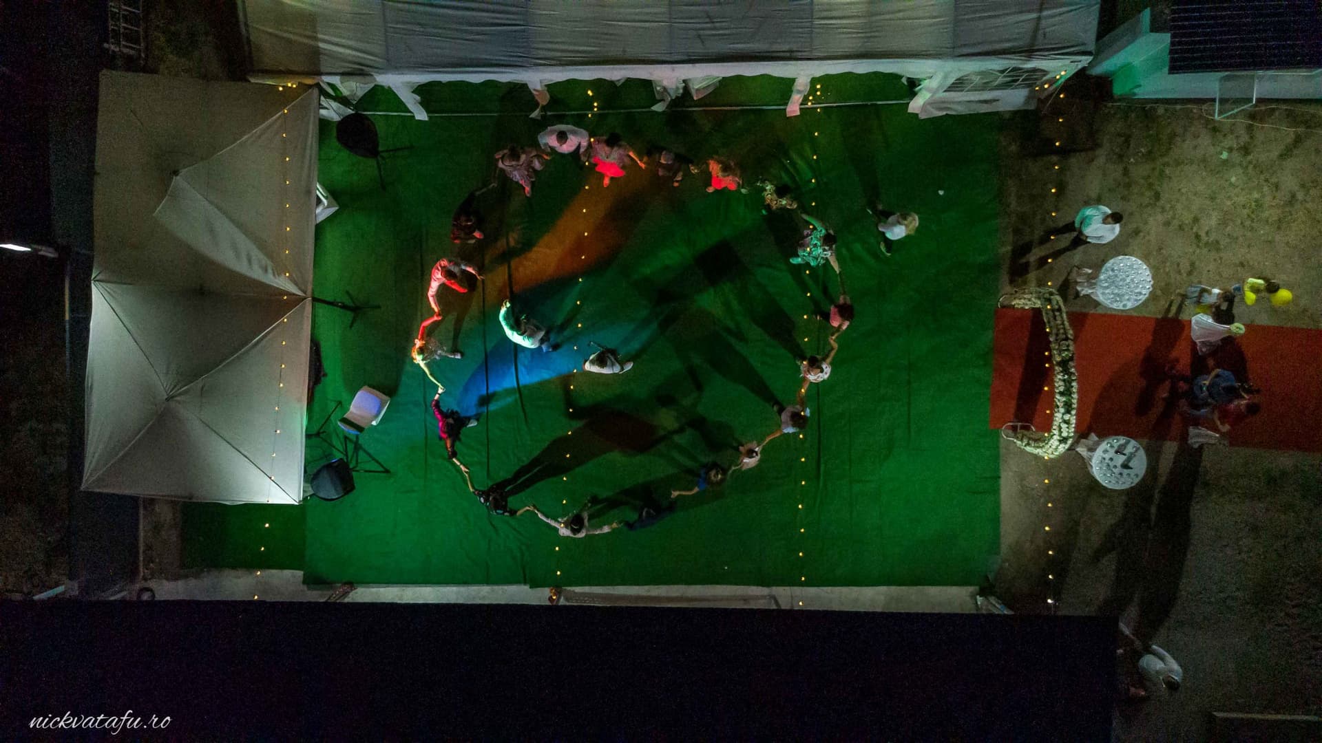 Grup de persoane dansând în cerc pe un covor verde, plin de emoție la un botez în Pitești, fotografie de eveniment.