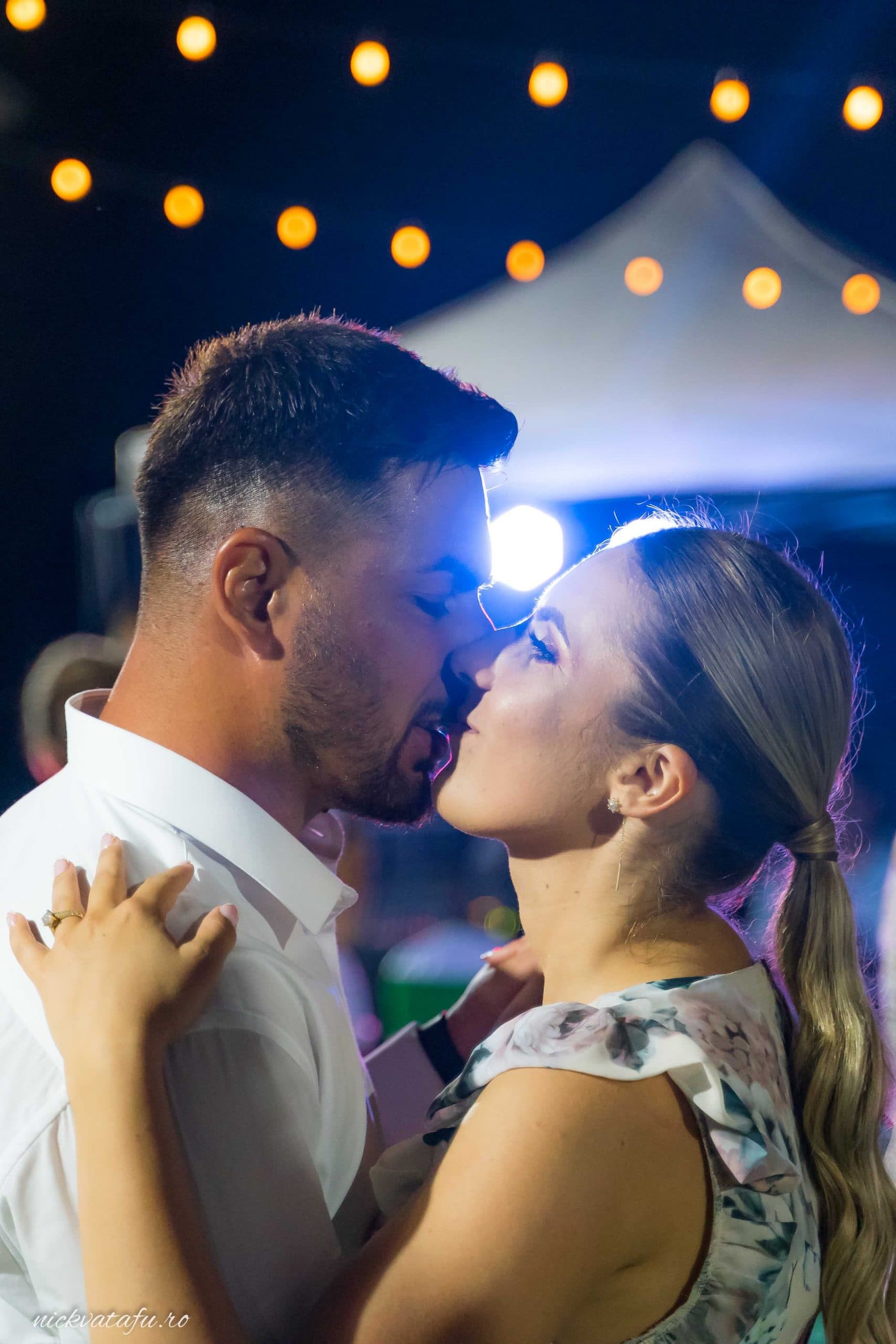 Cuplu dansând și împărtășind un sărut pasional, în atmosfera unei petreceri de nuntă plină de emoție.