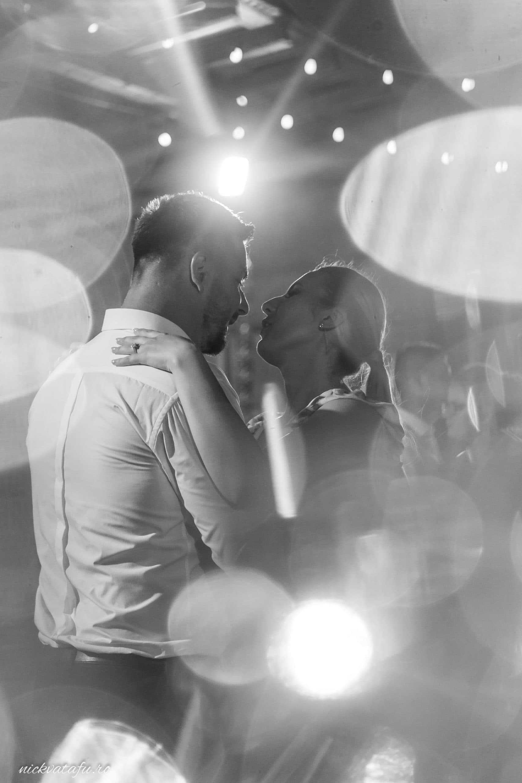 Mire și mireasă dansând emoționant sub lumini strălucitoare, fotografie de nuntă plină de intimitate.