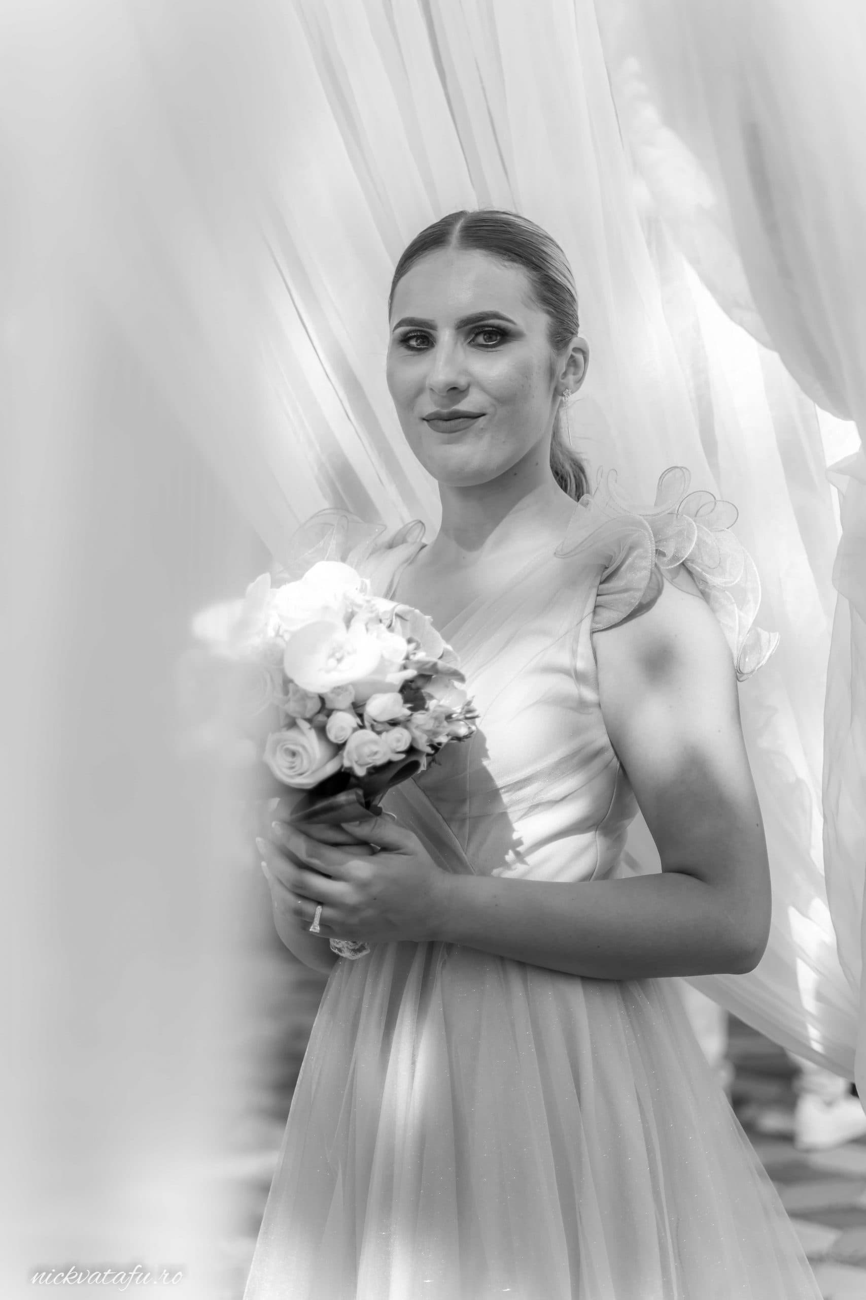 Mireasă elegantă cu buchet de flori, surprinsă într-un moment de reflecție înainte de ceremonie, detalii nuntă emoționante.