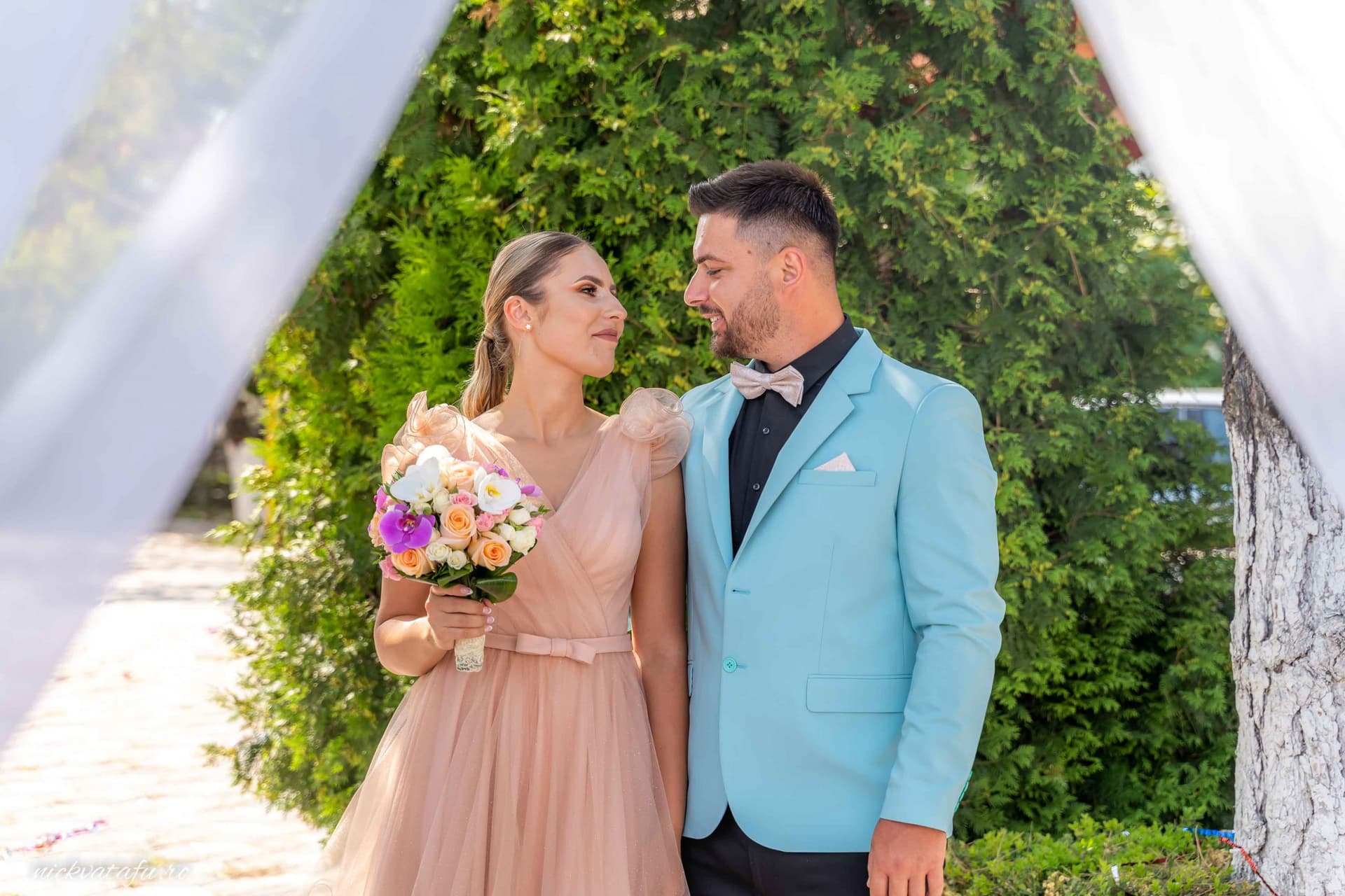 Mire și mireasă admirându-se cu emoție în fața unui fundal verde, fotografie de nuntă plină de iubire.