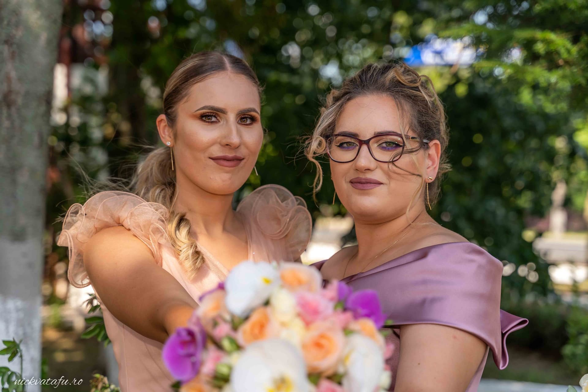 Două domnișoare de onoare zâmbesc fericite, ținând un buchet de flori colorate, fotografie nuntă plină de emoție.