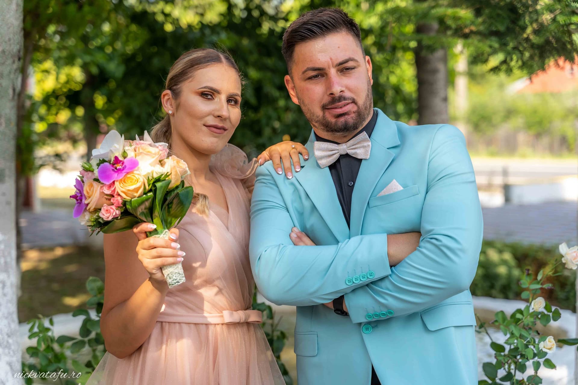 Cuplu elegant, zâmbind și pozând cu flori, într-o atmosferă de sărbătoare, detalii nuntă în natură.