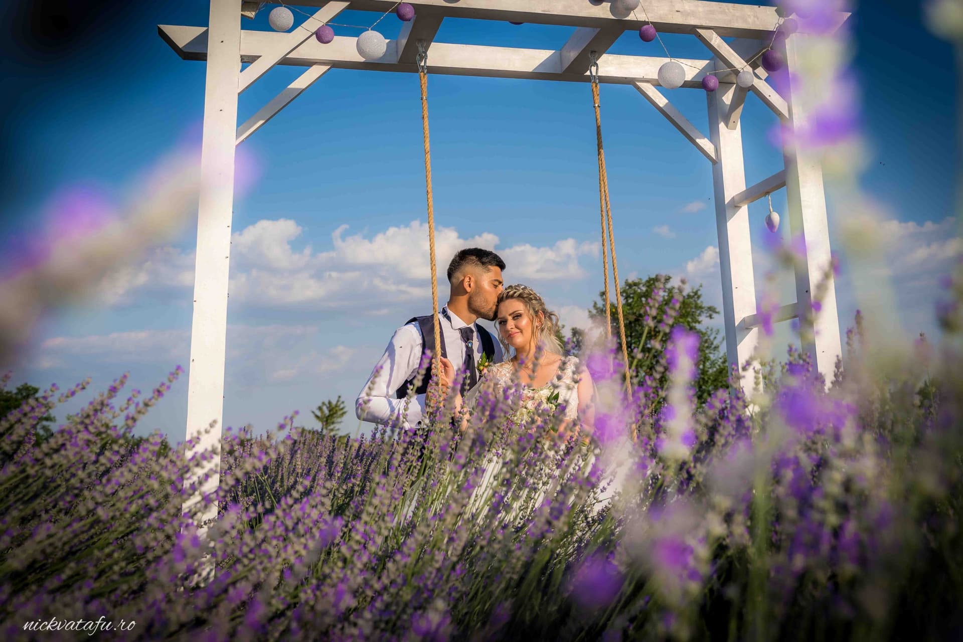 Mire și mireasă pe leagăn, înconjurați de lavandă, emanând emoție și fericire într-o fotografie de nuntă.